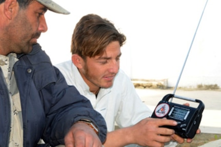 A young Afghan man and a border police officer search for the new Shinwar district radio station on a radio distributed by Afghan and coalition forces.