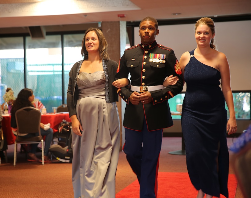 Sgt. Shawon Clark, supply, 4th Combat Engineer Battalion, escorts Lifestyle, Insights, Networking, Knowledge and Skills volunteers down the red carpet as they model proper ball attire during the Belle of the Ball event at the Officers’ Club, Oct. 4, 2014. After the event concluded, appropriate ball attire was given away.
