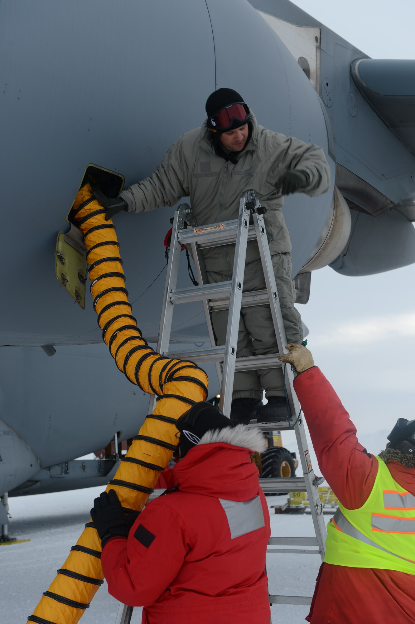 Tech. Sgt. JD Dearborn, 304th Expeditionary Airlift Squadron and 62nd Aircraft Maintenance Squadron flying crew chief, connects heating ducts, Oct. 8th, 2014, to the engine of a McChord Field C-17 Globemaster III aircraft at the Pegasus White Ice runway, part of McMurdo Station, Antarctica. Five different heating units were used to keep the aircraft from freezing up while it was being loaded as temperatures before wind chill were -19 degrees. (U.S. Air Force photo/Master Sgt. Todd Wivell)
