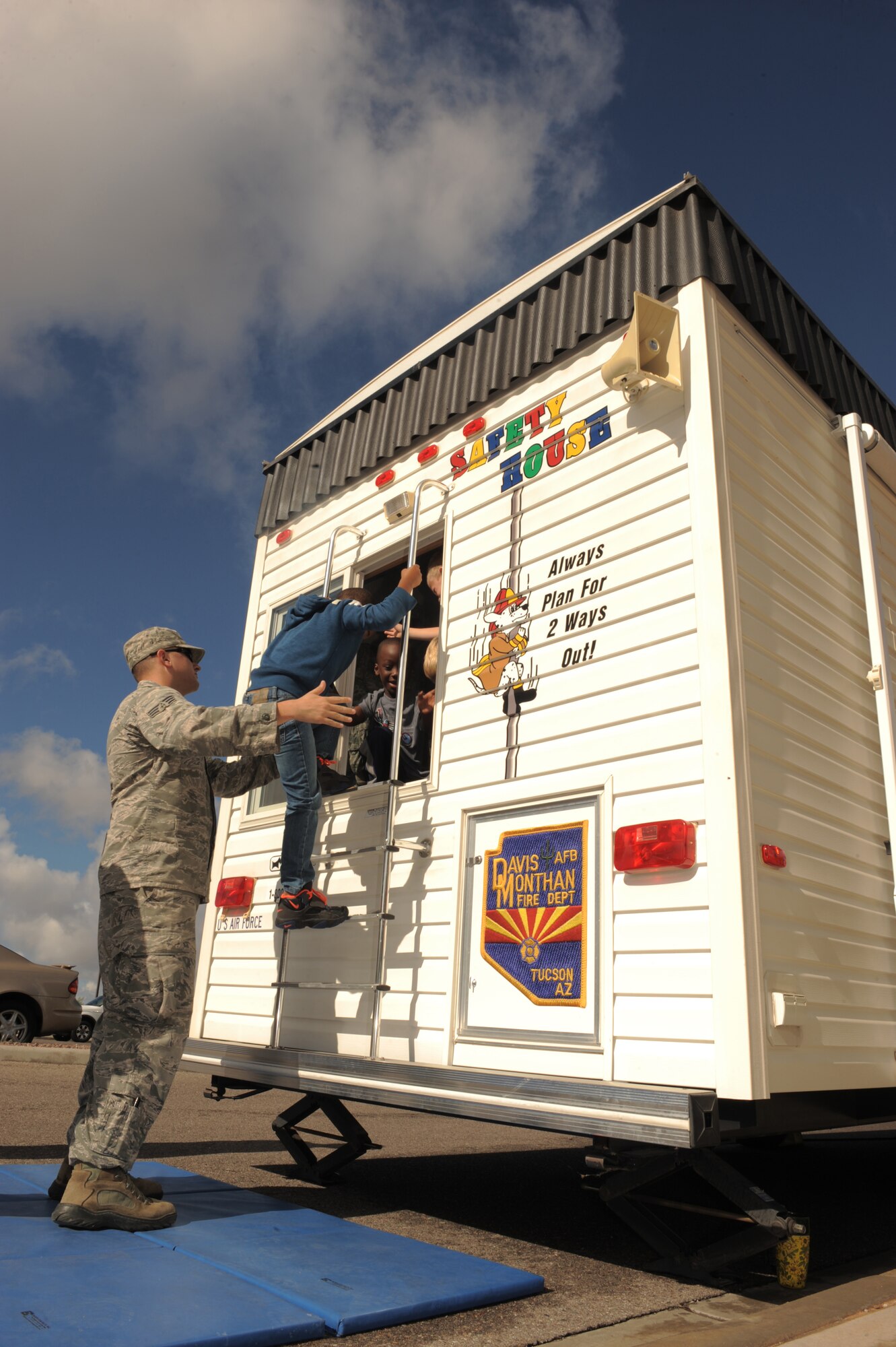 U.S. Air Force Senior Airman Christopher Ladue, 355th Fire Emergency Services firefighter, helps children from the School Age Program out of the window of a fire education trailer at Davis-Monthan Air Force Base, Ariz., Oct. 9, 2014. The fire education trailer is a simulated household environment intended to teach children how to identify fire hazards as well as how to safely evacuate a house in the event of a fire. (U.S. Air Force photo by Airman 1st Class Chris Drzazgowski/Released)