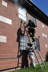 Airman 1st Class Jordan Patterson, 319th Civil Engineer Squadron firefighter apprentice, holds a ladder steady for Airman 1st Class Scott Miller, 319th CES firefighter apprentice, so that he can climb up to the smoke-filled window during a fire training exercise Oct. 8, 2014 at Grand Forks Air Force Base, N.D. The exercise took place during Fire Prevention Week, emphasizing the importance of fire prevention and safety.. (U.S. Air Force photo/Airman 1st Class Bonnie Grantham)
