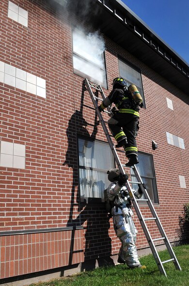 Airman 1st Class Jordan Patterson, 319th Civil Engineer Squadron firefighter apprentice, holds a ladder steady for Airman 1st Class Scott Miller, 319th CES firefighter apprentice, so that he can climb up to the smoke-filled window during a fire training exercise Oct. 8, 2014 at Grand Forks Air Force Base, N.D. The exercise took place during Fire Prevention Week, emphasizing the importance of fire prevention and safety.. (U.S. Air Force photo/Airman 1st Class Bonnie Grantham)