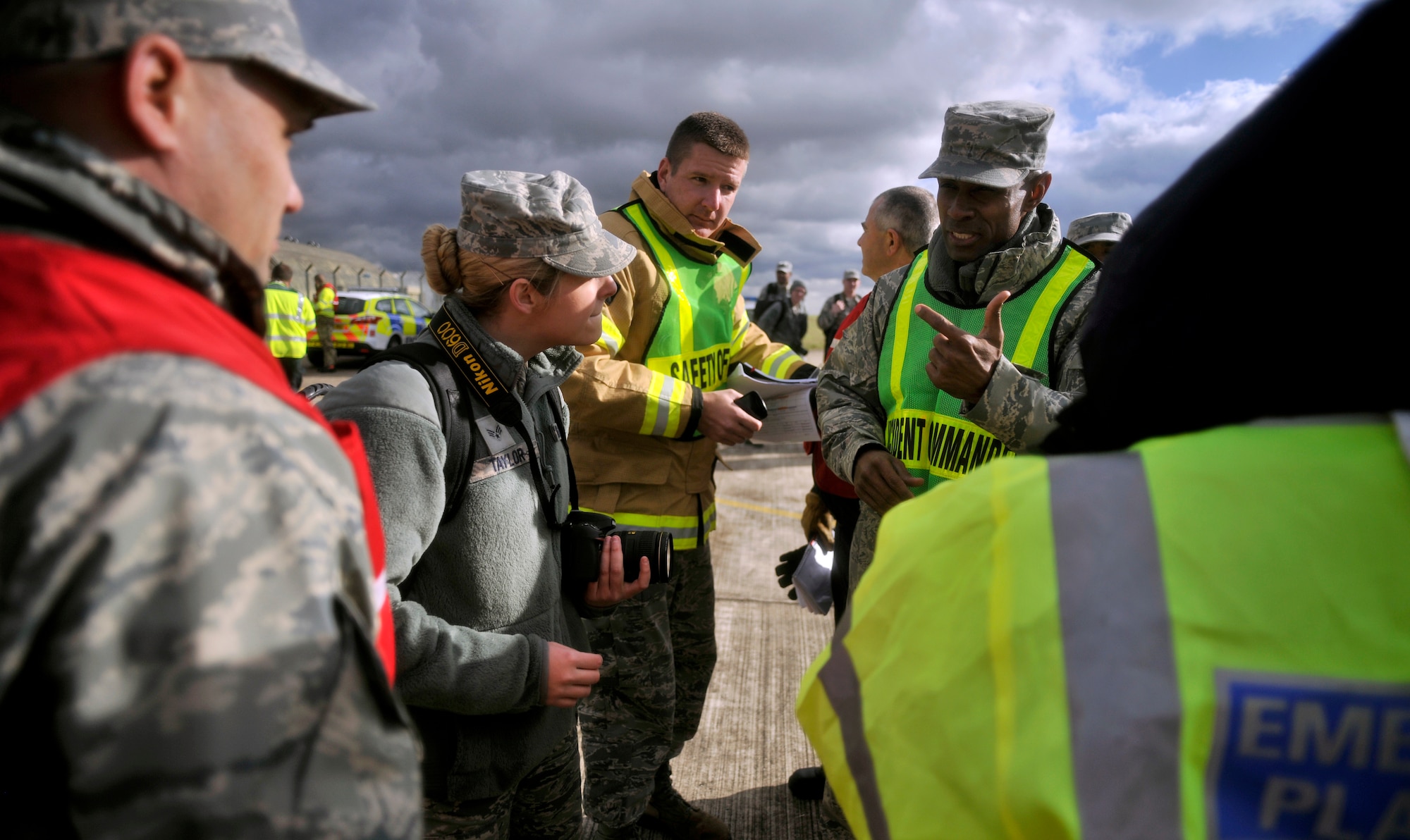U.S. Air Force Master Sgt. Dion Bullock, second from right, 100th Civil Engineer Squadron Fire Department deputy fire chief from Yuba City, Calif., speaks with Senior Airman Victoria Taylor, second from left, 100th Air Refueling Wing Public Affairs photojournalist from Lake Orion, Mich., regarding alert photography on scene during a Major Accident Response Exercise Oct. 7, 2014, at RAF Honington, England. During a major accident alert photo is called to the scene to document the aftermath. (U.S. Air Force photo/Senior Airman Christine Griffiths/Released)