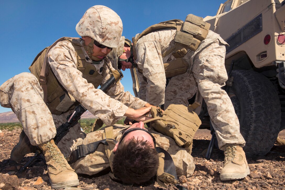 Navy Petty Officer 2nd Class Marlon Esmade, left, provides medical treatment to Marine Corps Cpl. Justin Edelbach, center, playing the role of a simulated casualty, during a convoy ambush exercise on a training range surrounding Yuma Proving Ground, Ariz., Oct. 2, 2014. Esmade is a corpsman and Edelbach is an automotive mechanic assigned to 3rd Battalion, 3rd Marine Regiment.
