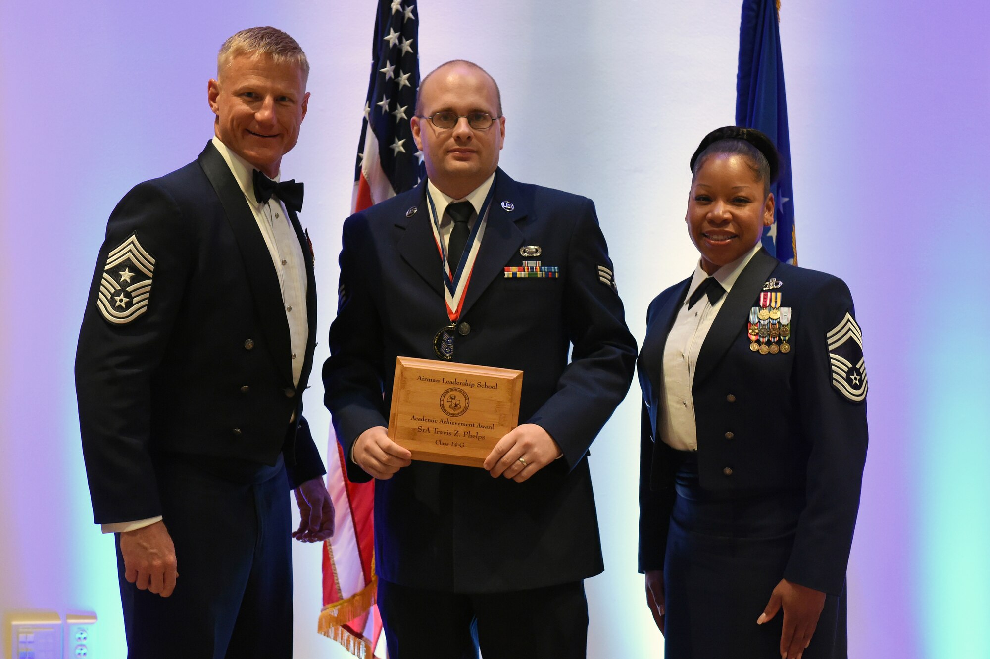 Senior Airman Travis Phelps, 566th Intelligence Squadron, center, receives the Academic Achievement Award during the Buckley Airman Leadership School Class 14-G graduation Oct. 9, 2014, at the Leadership Development Center on Buckley Air Force Base, Colo. This award is presented to the student with the highest overall average on all academic evaluations during ALS. (U.S. Air Force photo by Airman Emily E. Amyotte/Released)
