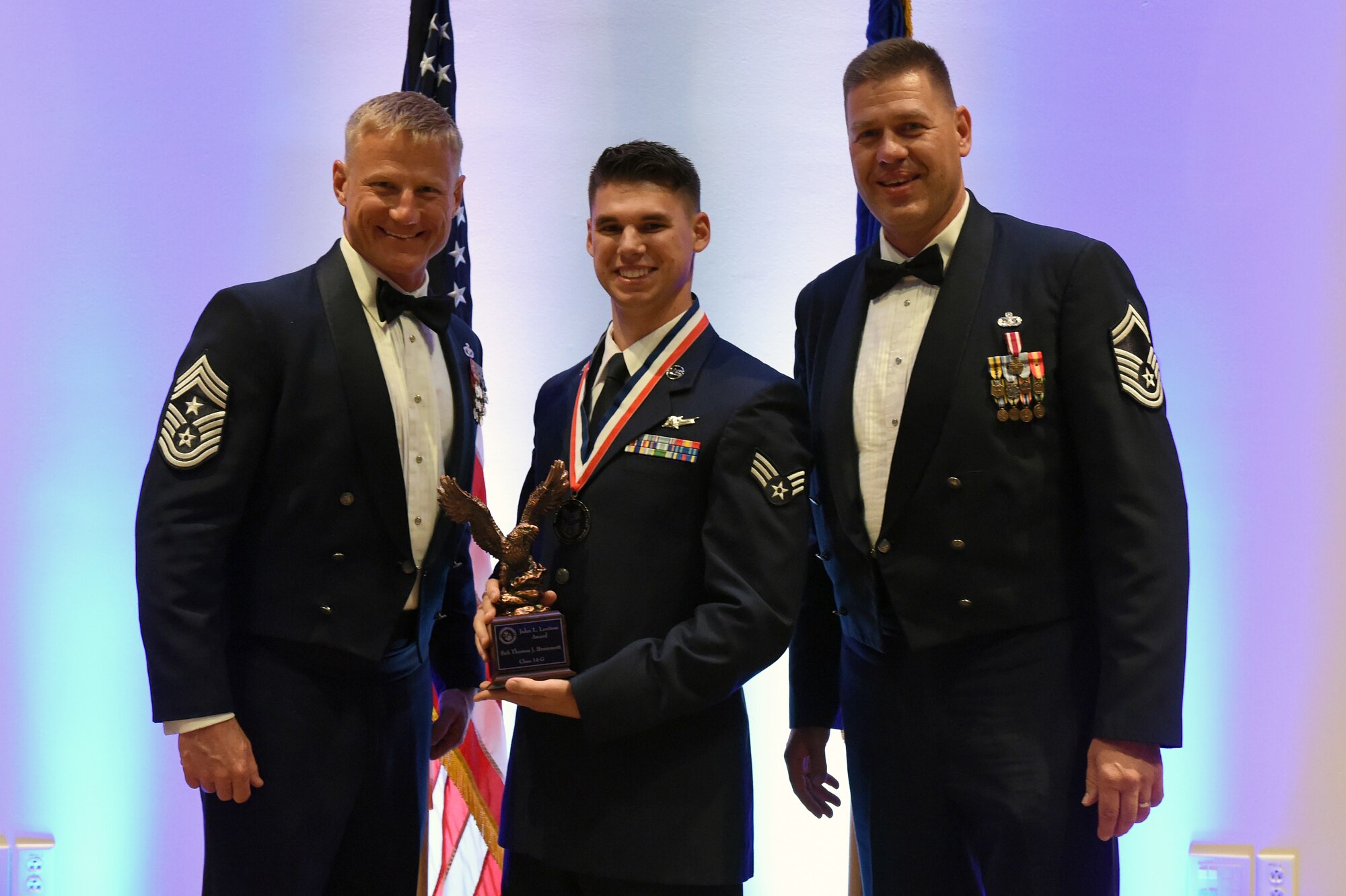 Senior Airman Thomas Brummett, 460th Operation Support Squadron instructor and mission crew chief, center, receives the John L. Levitow Award during the Buckley Airman Leadership School Class 14-G graduation Oct. 9, 2014, at the Leadership Development Center on Buckley Air Force Base, Colo. The Levitow Award is given to the ALS graduate with the highest academic scores and leadership potential. (U.S. Air Force photo by Airman Emily E. Amyotte/Released)