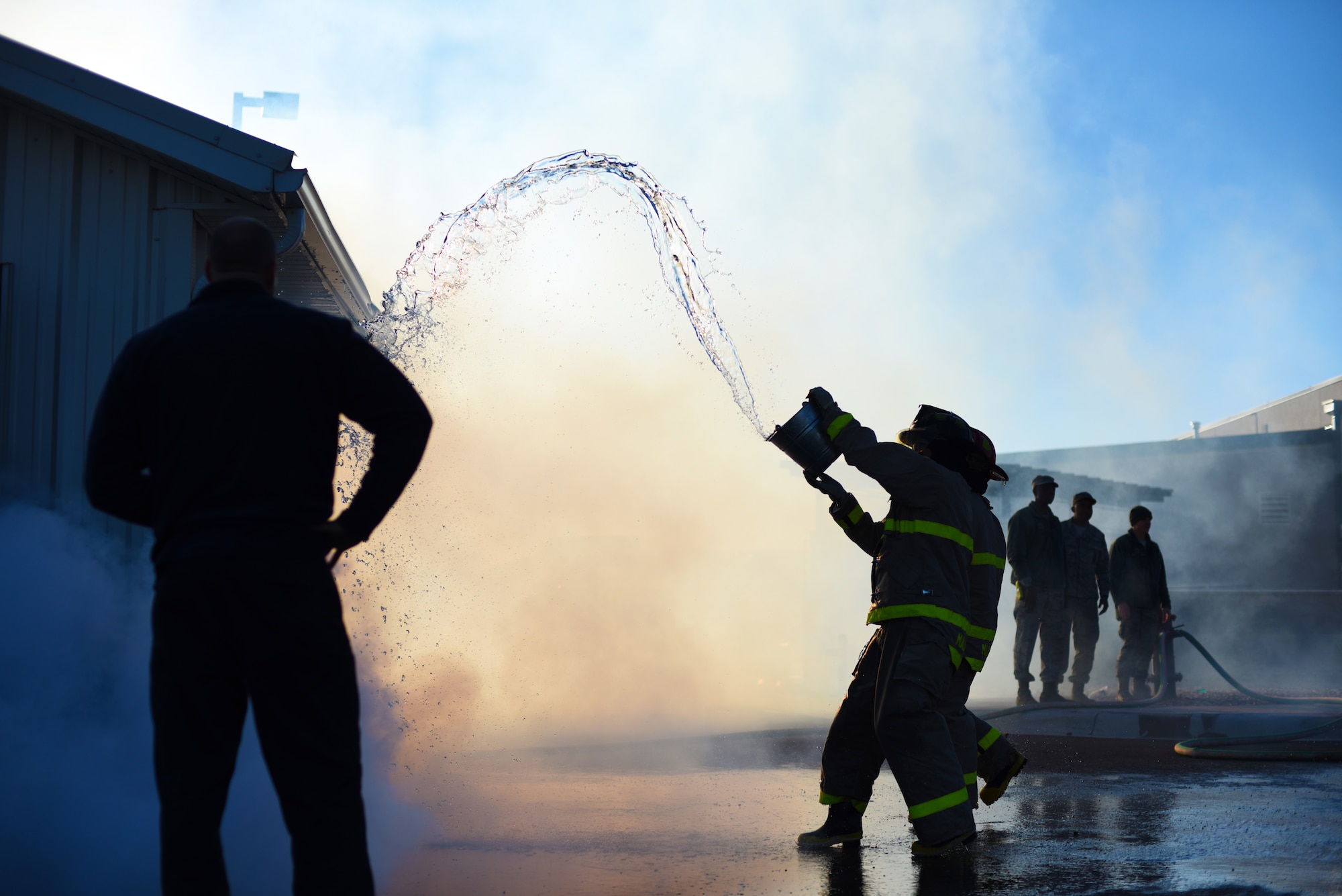 An Airman throws water onto a simulated burning building during Malmstrom Air Force Base’s fourth annual Fire Prevention Week fire muster Oct. 10. While completing this station, contestants were required to fill a 55-gallon drum by throwing water onto the roof of the structure and having the runoff drain into the barrel. (U.S. Air Force photo/Airman 1st Class Collin Schmidt)