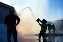 An Airman throws water onto a simulated burning building during Malmstrom Air Force Base’s fourth annual Fire Prevention Week fire muster Oct. 10. While completing this station, contestants were required to fill a 55-gallon drum by throwing water onto the roof of the structure and having the runoff drain into the barrel. (U.S. Air Force photo/Airman 1st Class Collin Schmidt)