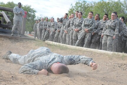 Staff Sgt. Dennis Weis, 323rd Training Squadron military training instructor, demonstrates how to complete one of the obstacles for trainees at the basic military training obstacle course, which included performing the low crawl, Sept. 24, 2014 at Joint Base San Antonio-Lackland,. The trainees completed the last run of course before its permanent closure the same day. A new course, called the Leadership Reaction Course, was added to basic expeditionary Airmen’s training, also known as BEAST week, at JBSA-Lackland Medina Annex and became fully operational Sept. 29. (U.S. Air Force photo by Senior Airman Krystal Jeffers/Released)