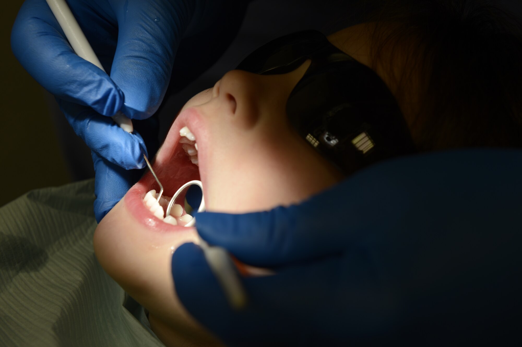 U.S. Air Force Staff Sgt. Ulices Pereira, 52nd Dental Squadron dental logistics NCO in charge, inspects the teeth of Miranda Wright, daughter of Sibel and U.S. Air Force Master Sgt. Nathan Wright, 52nd Medical Support Squadron, during a walk-in children dental clinic at Spangdahlem Air Base, Germany, Oct. 10, 2014. The 52nd DS will provide dental care to more than 100 children during its semi-annual walk-in clinic. (U.S. Air Force photo by Staff Sgt. Christopher Ruano/Released)