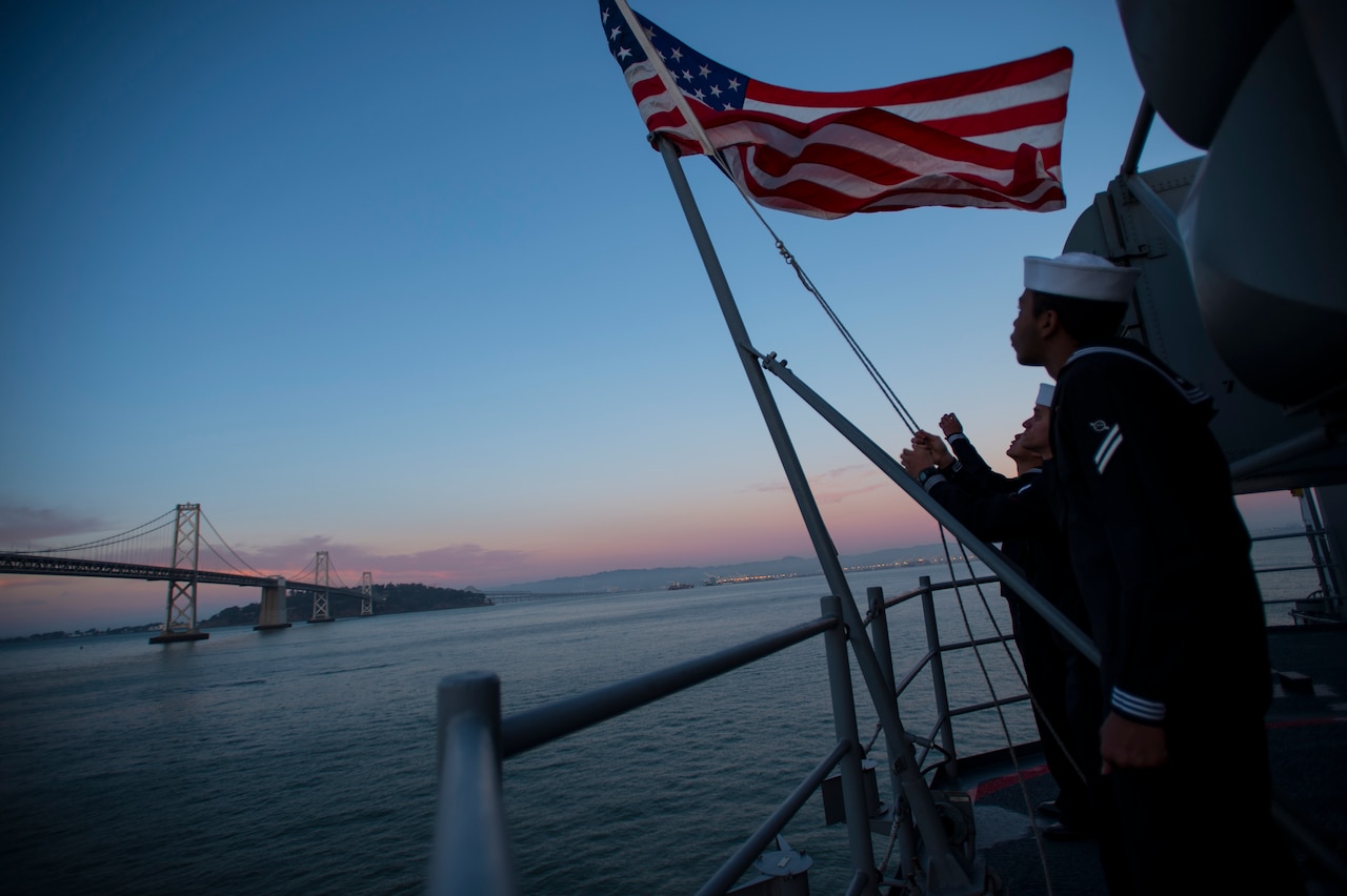 Sailors assigned to the future amphibious assault ship USS America perform evening colors on the ship's fantail while moored in San Francisco Bay Oct. 7, 2014, during San Francisco Fleet Week 2014. America is scheduled to be commissioned near the end of fleet week, Oct. 11. U.S. Navy photo by Petty Officer 1st Class Demetrius Kennon