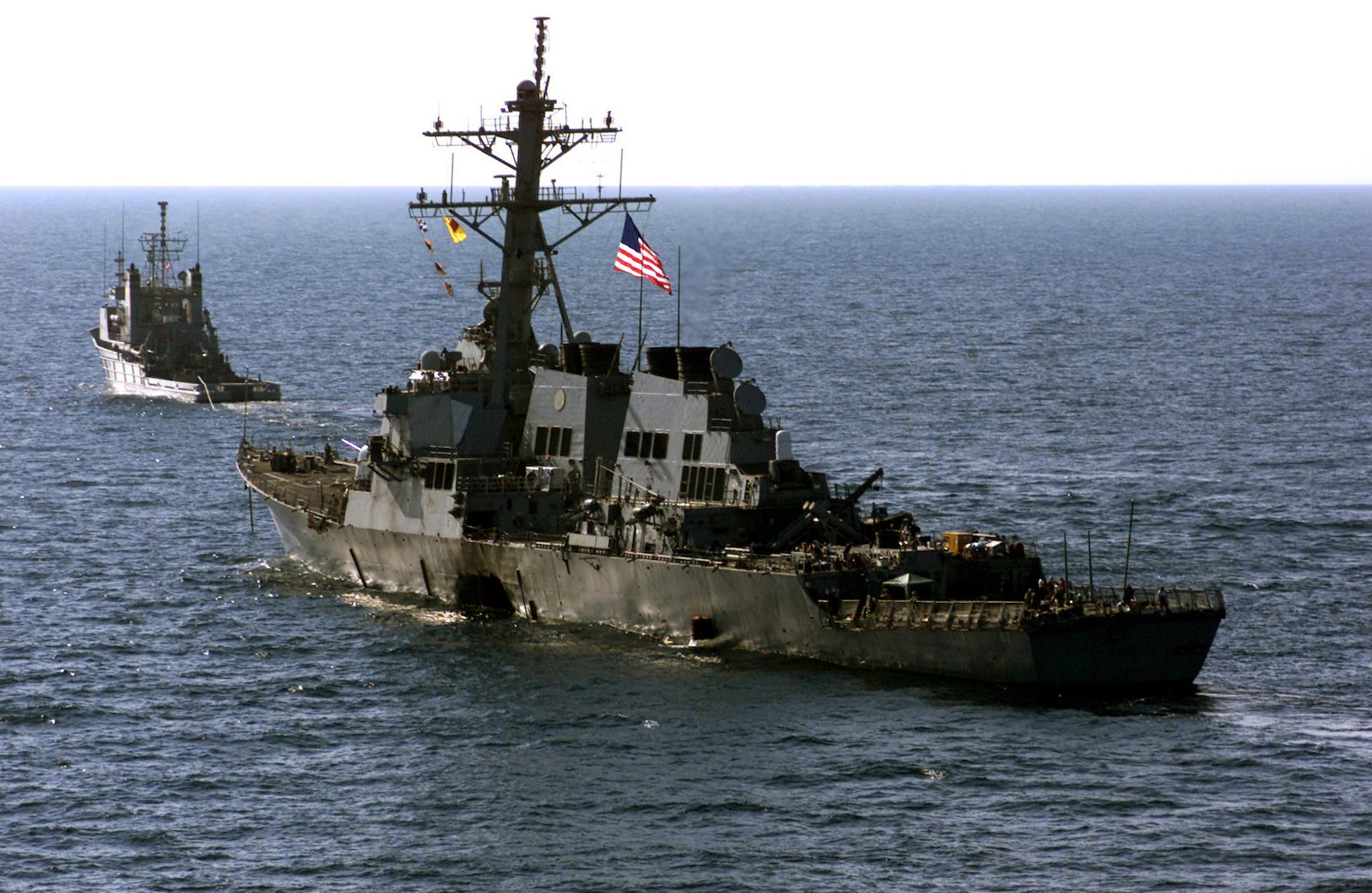 The Crew of the ARLIGH BURKE-class USS COLE (DDG 67), escort their wounded ship aboard Navy tug vessel, USNS CATAWBA, to a staging point in the Yemeni harbor of Aden awaiting transportation by the Norwegian-owned semi-submersible heavy lift ship MV BLUE MARLIN back to their homeport, during Operation DETERMINED RESPONSE, on October 29, 2000.  