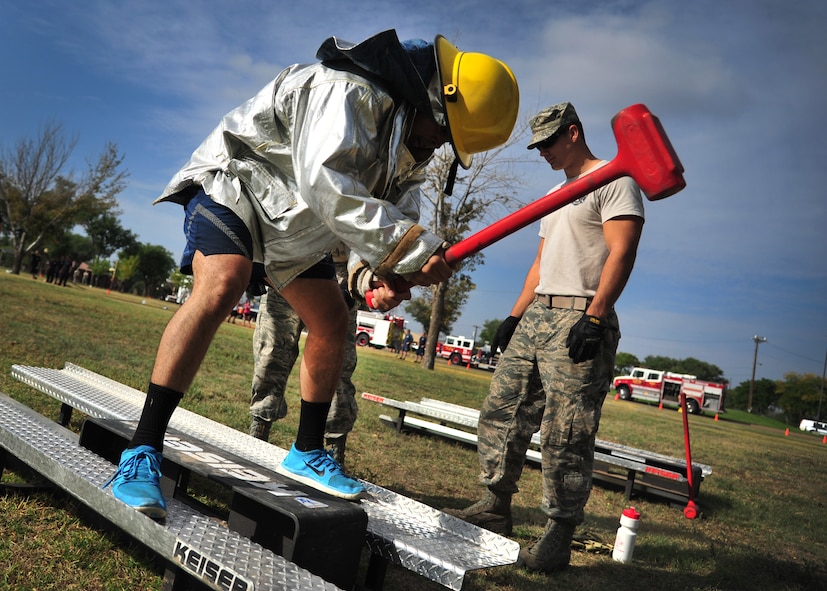 A U.S. Air Force airman struggles with a sledge hammer while a firefighter offers sideline coaching during the 15th Annual Squadron Fire Muster Oct. 9, 2014 at Cannon Air Force Base, N.M. The 27th Special Operations Civil Engineer Squadron hosts fellow Air Commandos each year during Fire Prevention Week to take part in friendly competition. (U.S. Air Force photo/Staff Sgt. Alexxis Pons Abascal)