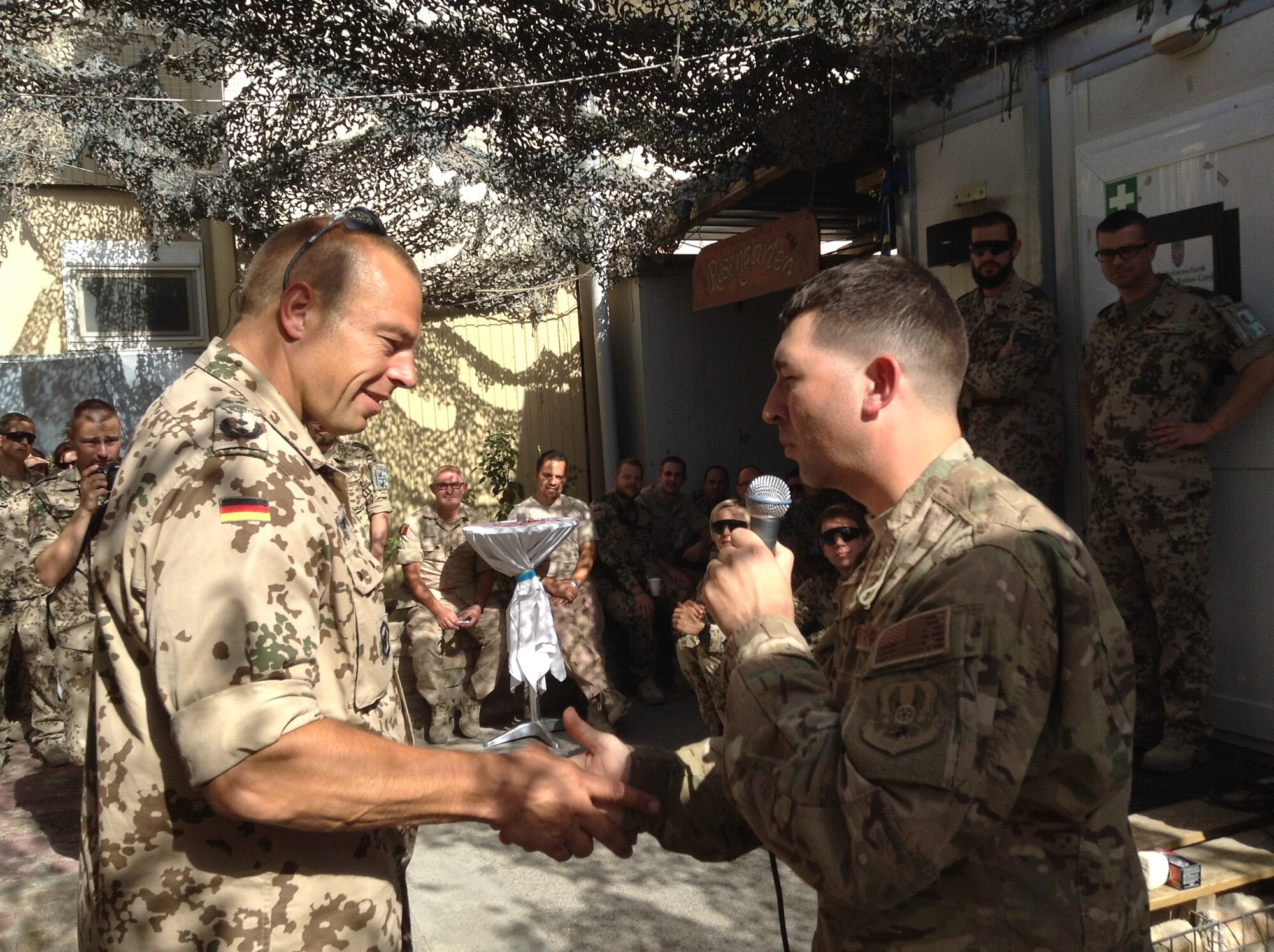 Capt Daniel W. Boothe, Officer in charge of the AFCENT Band, coins the director of the German Casualty Care Facility at Mazar-e-Sharif, Afghanistan, after the band’s strolling performance on Sept. 21, 2014.  The AFCENT Band performed at six forward operating bases in Afghanistan for more than 2,000 Airmen, joint and coalition forces during the month of September.  (U.S. Air Force Photo/Courtesy photo)