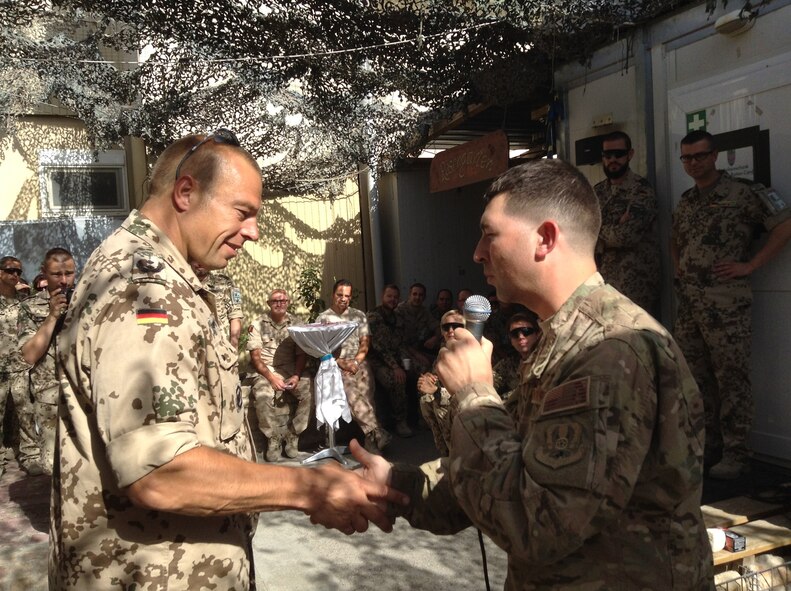 Capt Daniel W. Boothe, Officer in charge of the AFCENT Band, coins the director of the German Casualty Care Facility at Mazar-e-Sharif, Afghanistan, after the band’s strolling performance on Sept. 21, 2014.  The AFCENT Band performed at six forward operating bases in Afghanistan for more than 2,000 Airmen, joint and coalition forces during the month of September.  (U.S. Air Force Photo/Courtesy photo)