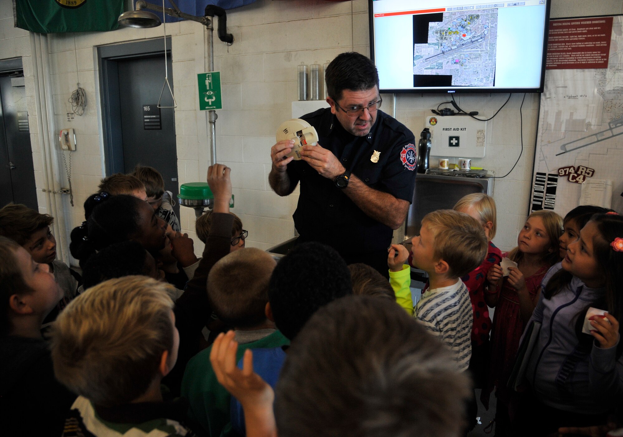 Craig Sayler, 92nd Civil Engineer Squadron firefighter, demonstrates how to properly test a smoke detector for students from Michael Anderson Elementary School during a tour of the fire department at Fairchild Air Force Base, Washington, Oct. 6, 2014. The tour was one of several events held during Fire Prevention Week 2014 to bring awareness to fire safety and prevention. (U.S. Air Force photo by Senior Airman Mary O'Dell)
