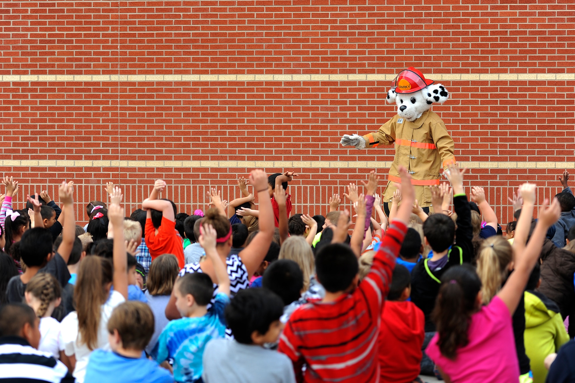 SAN ANGELO, Texas – Lamar Elementary School students raise their hands to participate in a demonstration with Sparky, Goodfellow Fire Department mascot, at Lamar Elementary School Oct. 6. Sparky showed the children how to safely crawl to the nearest exit in an emergency fire situation. (U.S. Air Force photo/ Airman 1st Class Devin Boyer)