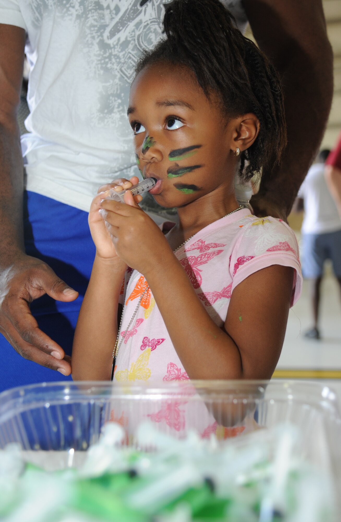 The daughter of Staff Sgt. Loren King, 81st Diagnostic and Therapeutics Squadron, drinks juice from a medicine tube which simulates receiving an immunization during Operation Hero Oct. 11, 2014, at Keesler Air Force Base, Miss.  The event was designed to help children better understand what happens when their parents deploy.  (U.S. Air Force photo by Kemberly Groue)