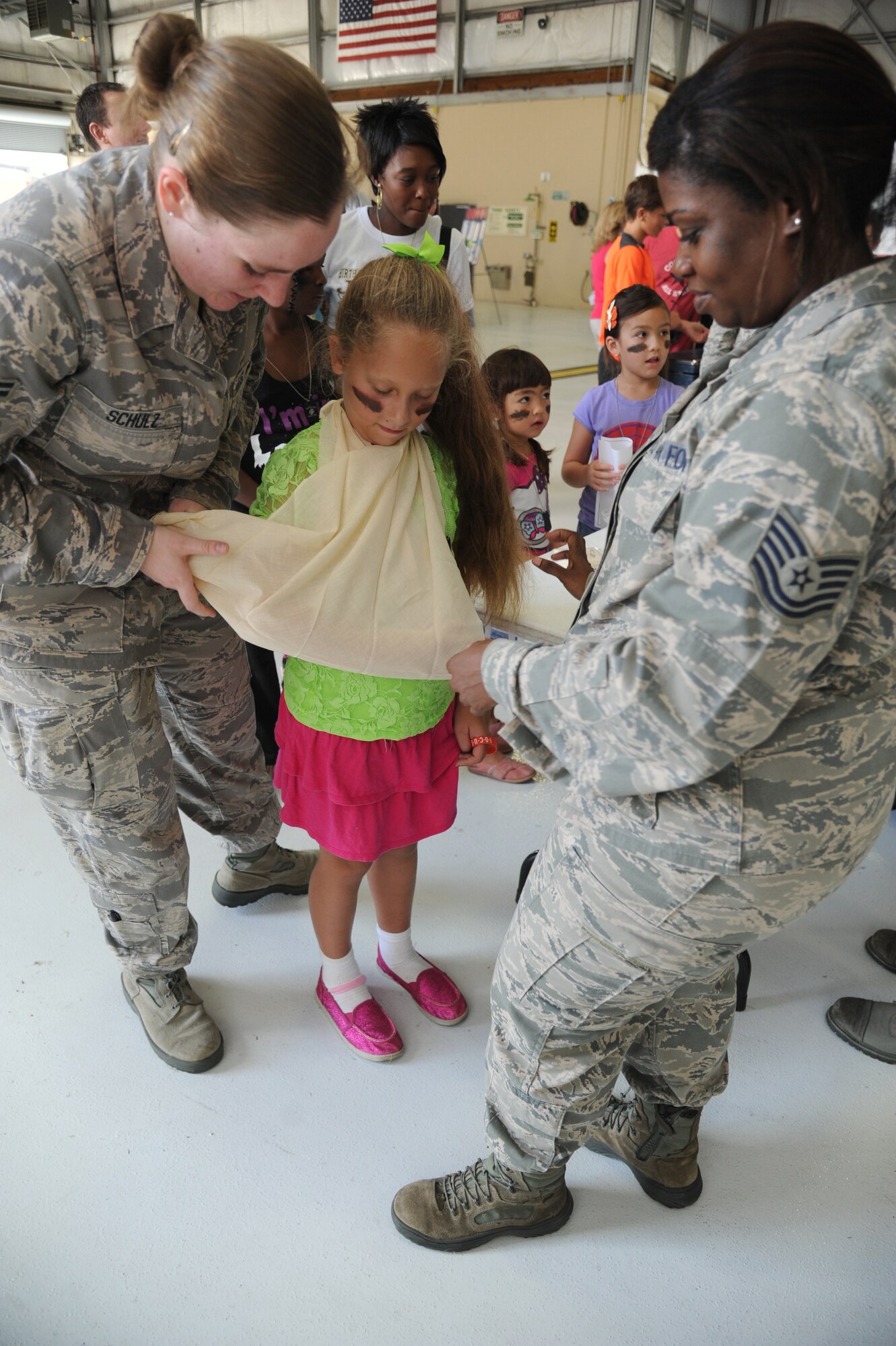 Airman 1st Class Jeanette Schulz and Tech. Sgt. Tiffany Cunningham, 81st Medical Operations Squadron, demonstrate how to make an arm sling on the daughter of Capt. Jarrett Eyer, 81st Surgical Operations Squadron, during Operation Hero Oct. 11, 2014, at Keesler Air Force Base, Miss.  The event was designed to help children better understand what happens when their parents deploy.  (U.S. Air Force photo by Kemberly Groue)