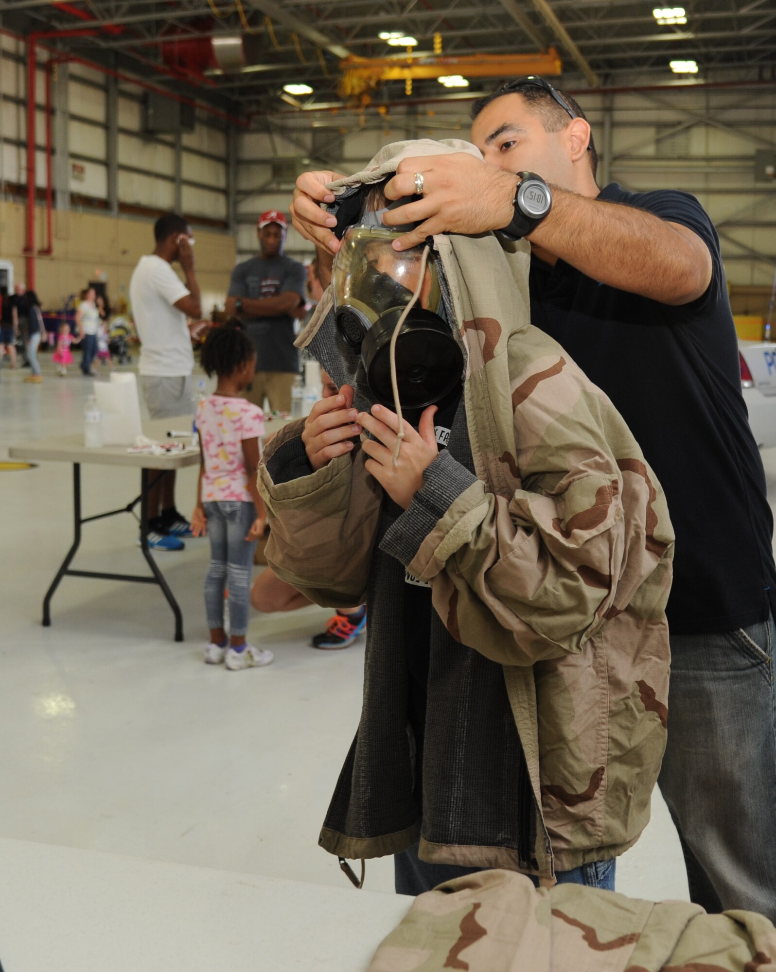 Tech. Sgt. Gilbert Barrera, 333rd Training Squadron, fits a gas mask and uniform on the son of  Lt. Col. Teresa Roberts, 81st Aerospace Medicine Squadron commander, during Operation Hero Oct. 11, 2014, at Keesler Air Force Base, Miss.  The event was designed to help children better understand what happens when their parents deploy.  (U.S. Air Force photo by Kemberly Groue)