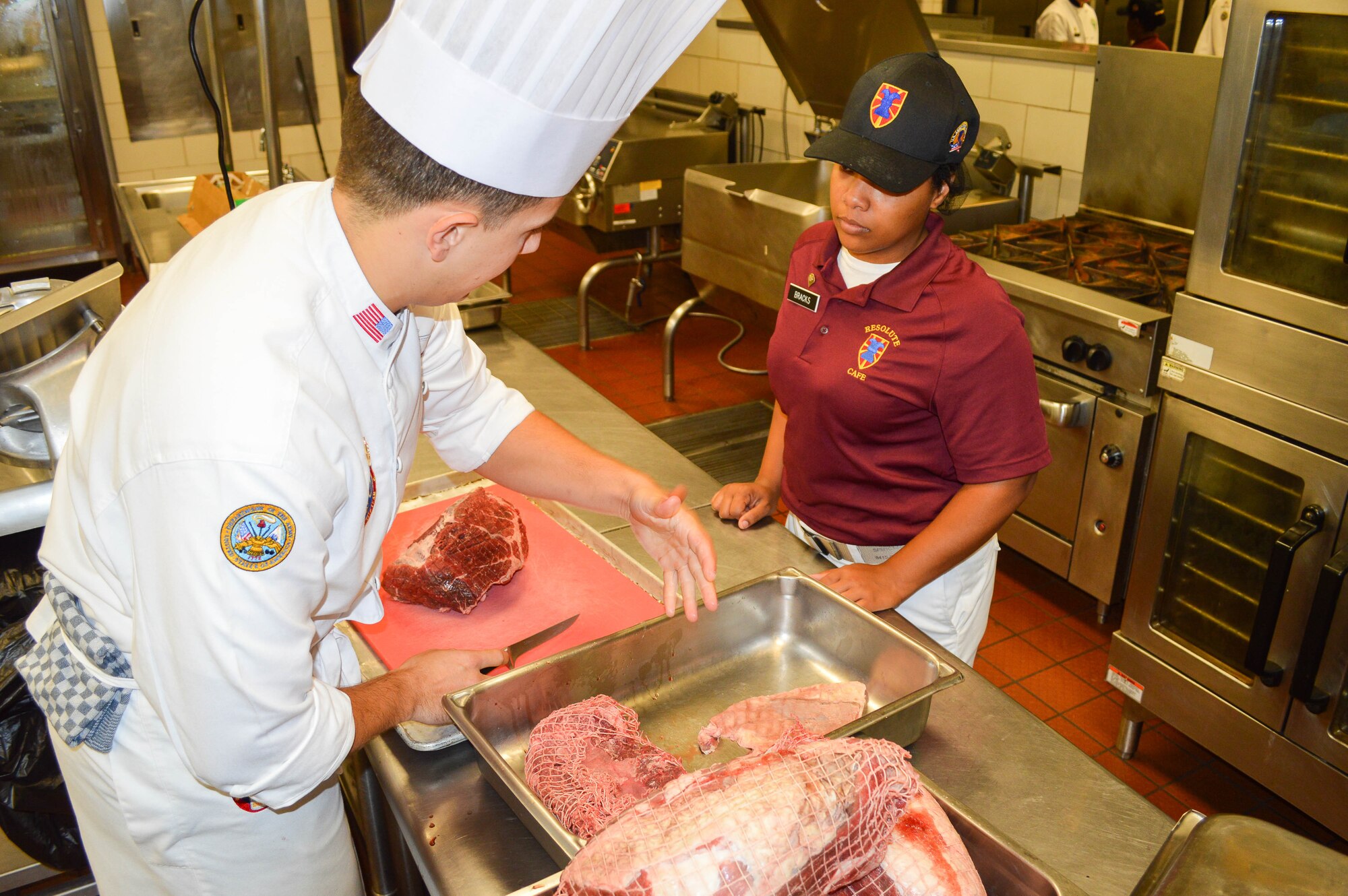 U.S. Army Staff Sgt. Billy Daugette III, Joint Culinary Center of Excellence instructor, shows Spc. Jimesha Bracks, 155th Inland Cargo Transfer Company, 53rd Transportation Battalion Movement Control, 7th Transportation Brigade (Expeditionary) culinary specialist, how to save time preparing food at Fort Eustis, Va., Oct. 1, 2014. Daugette collaborated with Bracks to prepare stuffed beef rolls and other dishes for the lunch menu. (U.S. Army photo by Spc. Marian Alleva/Released)
