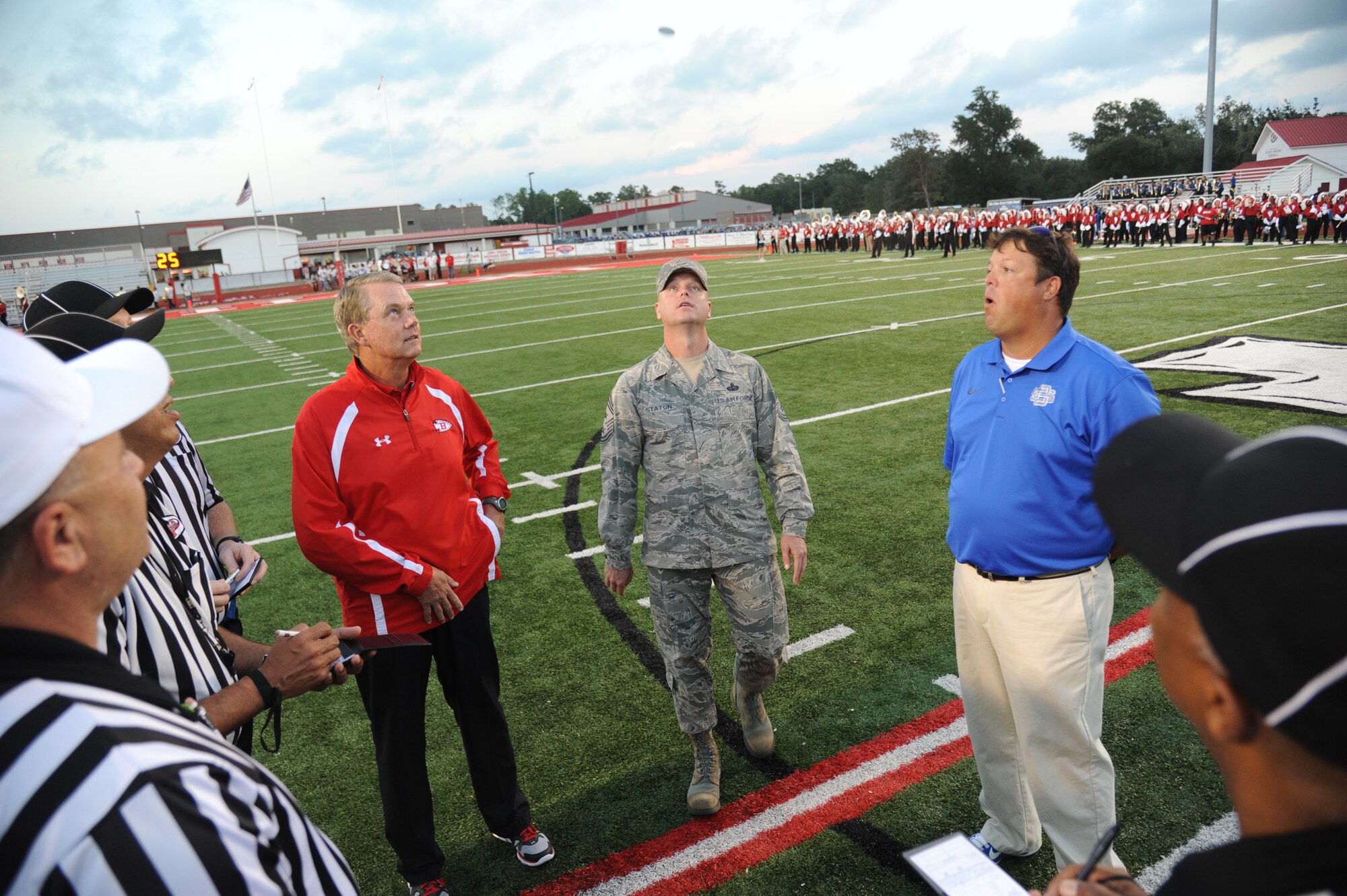 Chief Master Sgt. David Staton, 2nd Air Force command chief, tosses the coin for the official coin toss as the head coaches and referee staff watch closely during the Biloxi High School football game against Ocean Springs High School Oct. 10, 2014, at the Biloxi football stadium. Staton tossed the coin to determine which team would receive the ball first.  Ocean Springs defeated Biloxi 35-21.  (U.S. Air Force photo by Kemberly Groue)