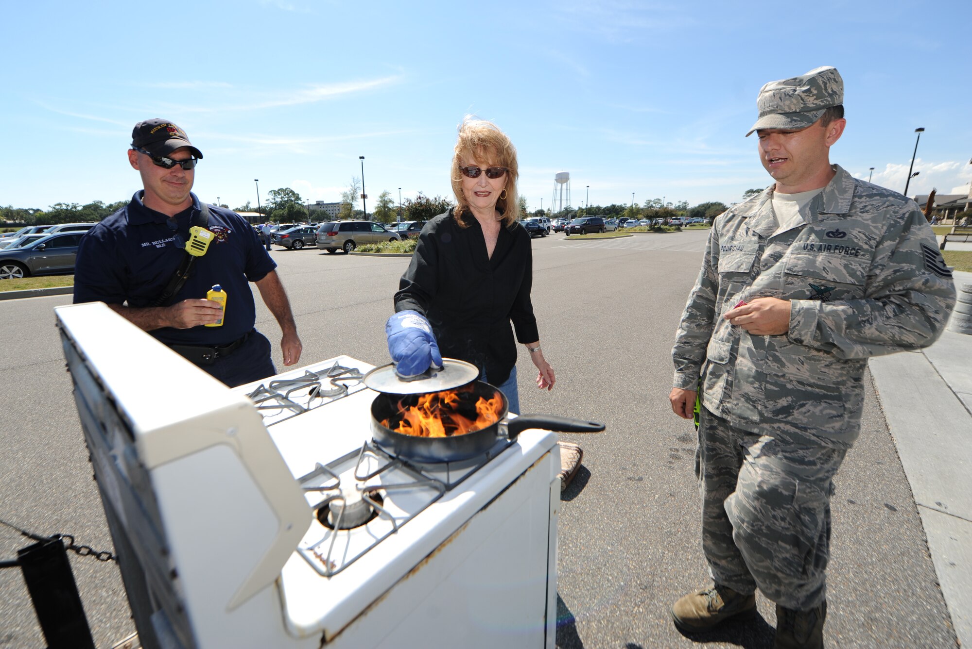 The wife of retired Senior Master Sgt. Jerry Wisniewski demonstrates how to safely put out a stove fire with Jerame Bullard and Tech. Sgt. Kyle Pourciau, 81st Infrastructure Division firefighters, Oct. 8, 2014, outside of the Commissary at Keesler Air Force Base, Miss.  Throughout fire prevention week the Keesler Fire Department conducted random fire drills, toured various facilities with Sparky the Fire Dog, passed out fire safety handouts and fire hats for children and provided stove and fire extinguisher demonstrations.  The week–long event ended with an open house at the fire station 10 a.m. to 2 p.m. Oct. 13.  (U.S. Air Force photo by Kemberly Groue)