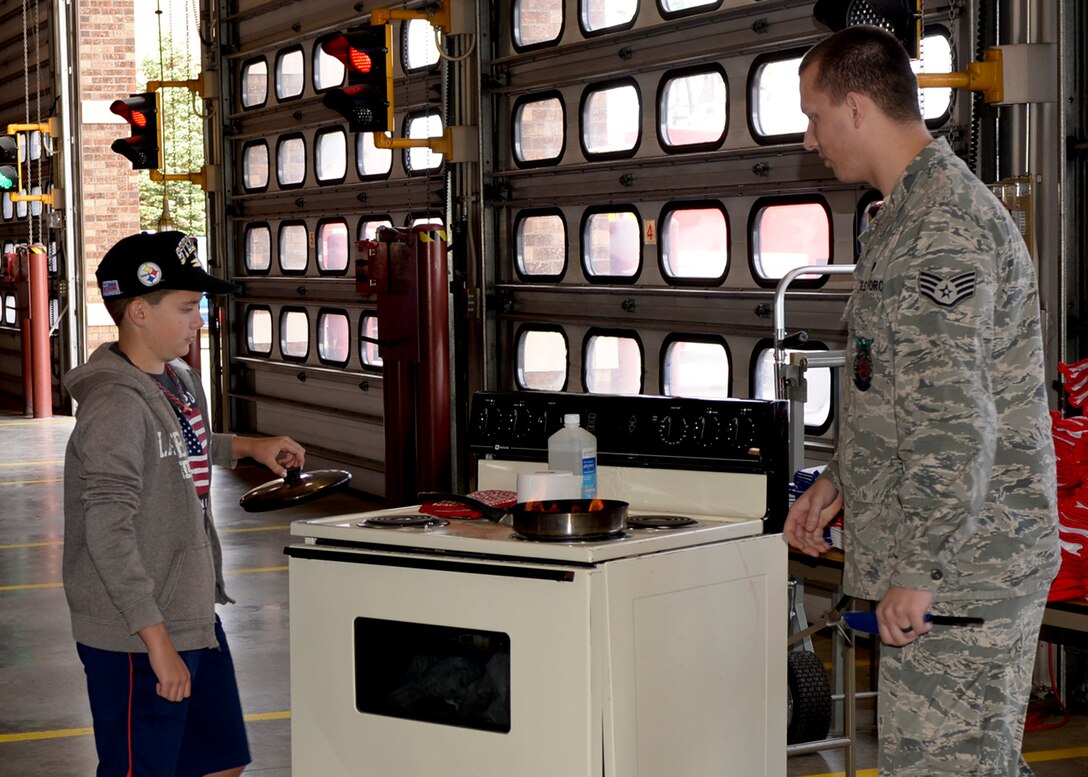 Staff Sgt. Brian Dvorak, 28th Civil Engineer Squadron firefighter, teaches children how to properly and safely handle a stove top fire during a National Fire Prevention Week open house at Ellsworth Air Force Base, S.D., Oct. 4, 2014. This year’s theme focuses on testing your fire alarms monthly to save lives and included a firefighter challenge event, a parade through base housing, and firefighters visiting area schools to talk about fire safety.  (U.S. Air Force photo by Senior Airman Anania Tekurio/Released)