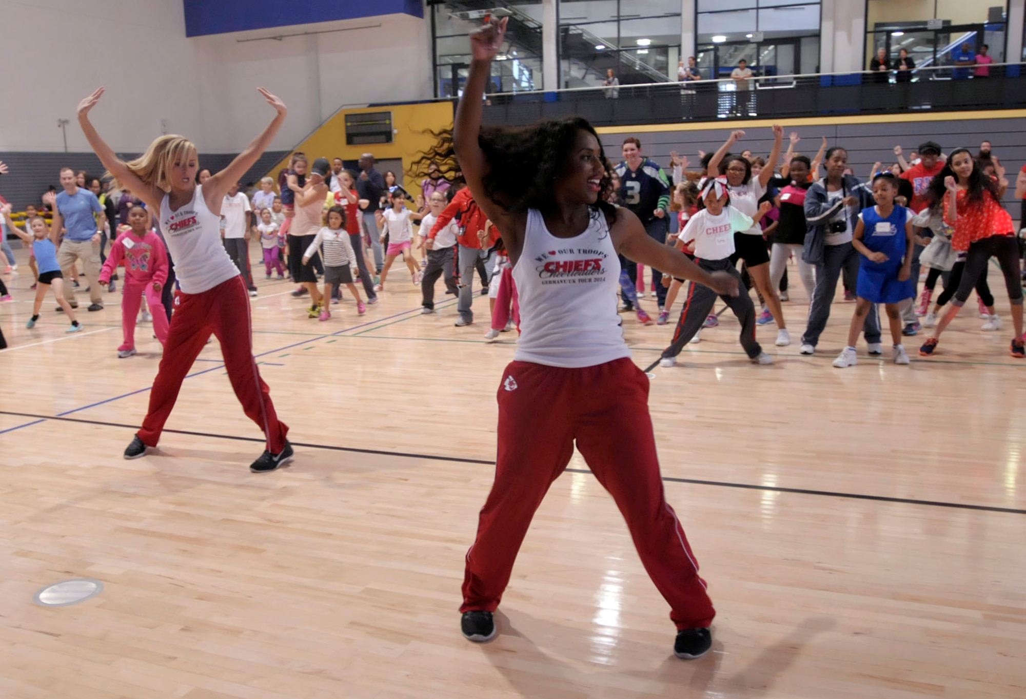 Kansas City Chiefs’ cheerleaders Krystal (front) and Hayley lead children and parents of the Kaiserslautern Military Community in a dance during a cheerleading clinic at the Southside Fitness Center on Ramstein Air Base, Germany, Oct. 11, 2014. The cheerleaders participated in the clinic as a way to say thank you and show their support the men and women of the U.S. Armed Forces and their families. (U.S. Air Force photo/Senior Airman Timothy Moore)
