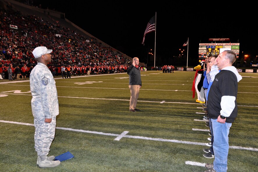 Master Sgt. Dartanion Pittrell, a line recruiter assigned to the 910th Airlift Wing Air Force Reserve Recruiting Flight, watches as Col. James Dignan, 910th Airlift Wing commander administers the oath enlistment to nine of the wing’s newest Citizen Airmen in an on-field ceremony in front of a crowd of more than 12,000 football fans at Stambaugh Stadium here, October 11, 2014. The ceremony took place between the first and second quarters of the game during which a group from nearby Youngstown Air Reserve Station, Ohio witnessed the YSU Penguins 1-AA team fall to the Western Illinois Leathernecks, 30-24. Earlier in the afternoon, more than 80 football fans representing the wing’s Citizen Airmen, along with their coworkers, families and friends enjoyed a tailgate picnic on a cool but sunny fall afternoon. The event, which has become a fall tradition in recent years for YARS personnel, was presented by the Youngstown Air Reserve Base-Community Council and the USO of Northern Ohio. The 910th Force Support Squadron Outdoor Recreation Office and Community Activity Center staff also supported the event. U.S. Air Force photo by Master Sgt. Bob Barko Jr.