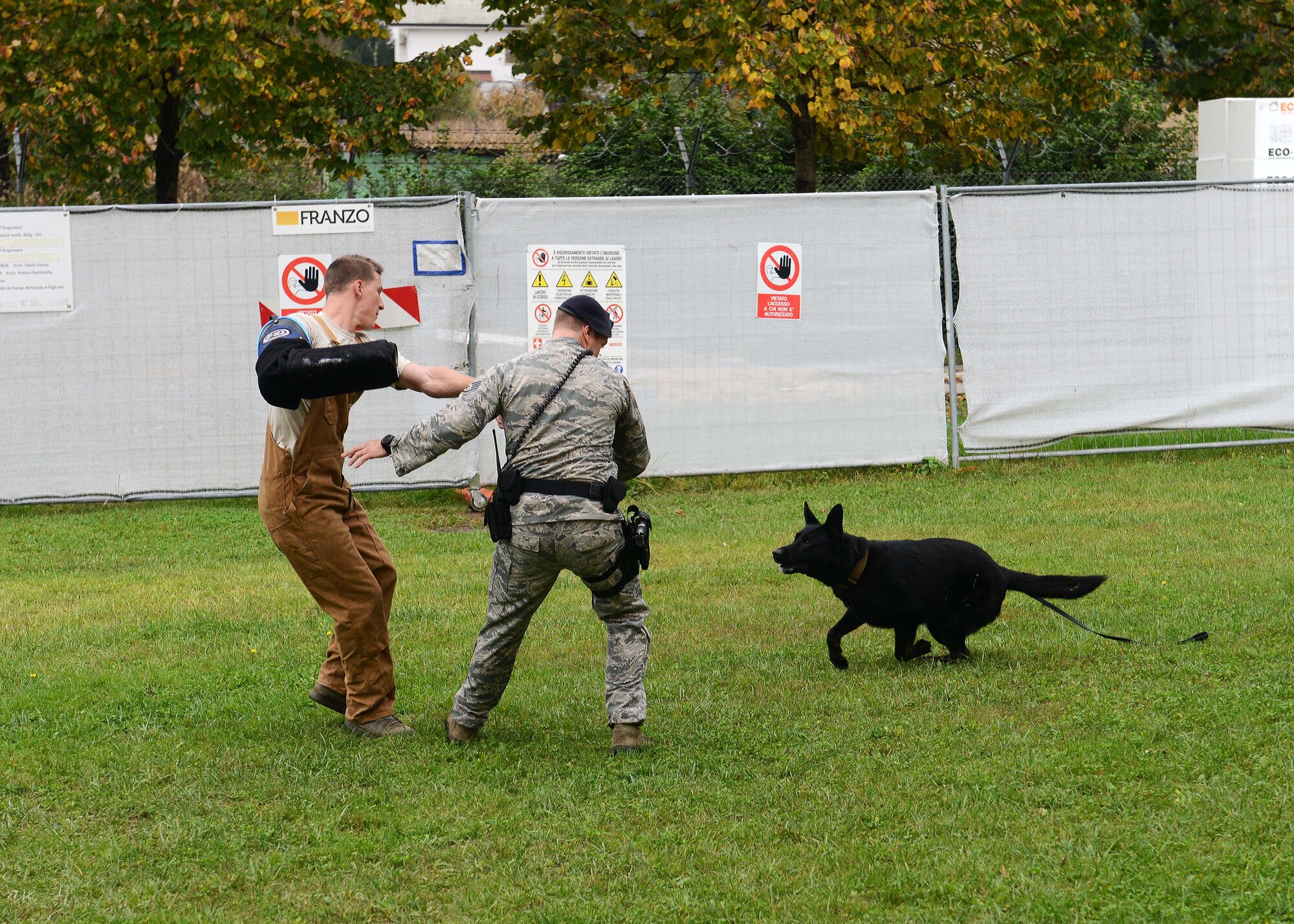 (From left) Staff Sgt. Andrew Healy braces himself while Staff Sgt. Erik Parris demonstrats the levels of aggression with Dox, a military working dog, during the first “AviCon,” Oct. 11, 2014, at Aviano Air Base, Italy. AviCon was hosted by Aviano’s Wing Diversity Council, which was created to support the Air Force diversity initiative. Both Healy and Parris are 31st Security Forces Squadron MWD handlers. (U.S. Air Force photo/Airman 1st Class Deana Heitzman) 