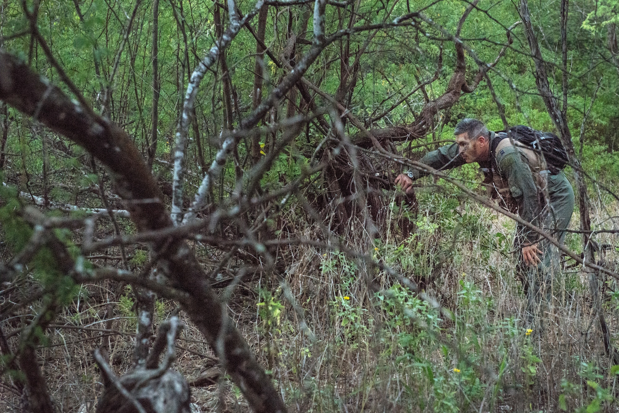 An aircrew member maneuvers through a wooded area while escaping capture during a combat survival refresher course Oct. 9, 2014, at Joint Base Pearl Harbor-Hickam, Hawaii. The survival, evasion, resistance and escape combat survival refresher course is designed to familiarize aircrew members with combat skills learned through hands-on training in a realistic environment. SERE is a program that provides training in evading capture, survival skills and the military code of conduct. (U.S. Air Force photo/Staff Sgt. Christopher Hubenthal)