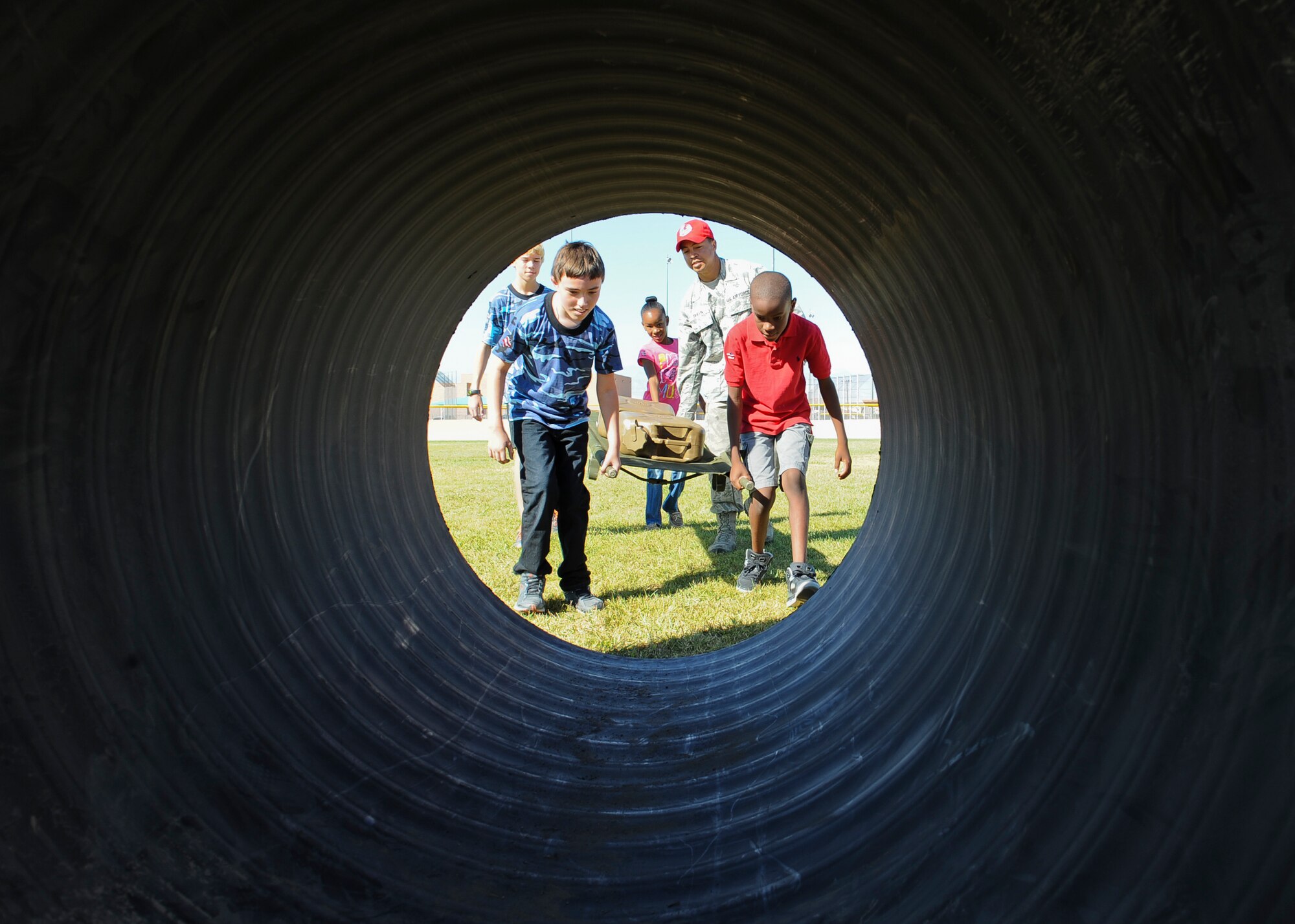 Staff Sgt. Theron Griffin, 820th RED HORSE heavy equipment operator, guides children into a tunnel on the obstacle course during the Nellis and Creech Kids Deployment at Nellis Air Force Base, Nev., Oct. 11, 2014. Children had to work as a team to carry a litter with water containers through an obstacle course to simulate carrying an injured person during a deployment. (U.S. Air Force photo by Staff Sgt. Victoria Sneed)
