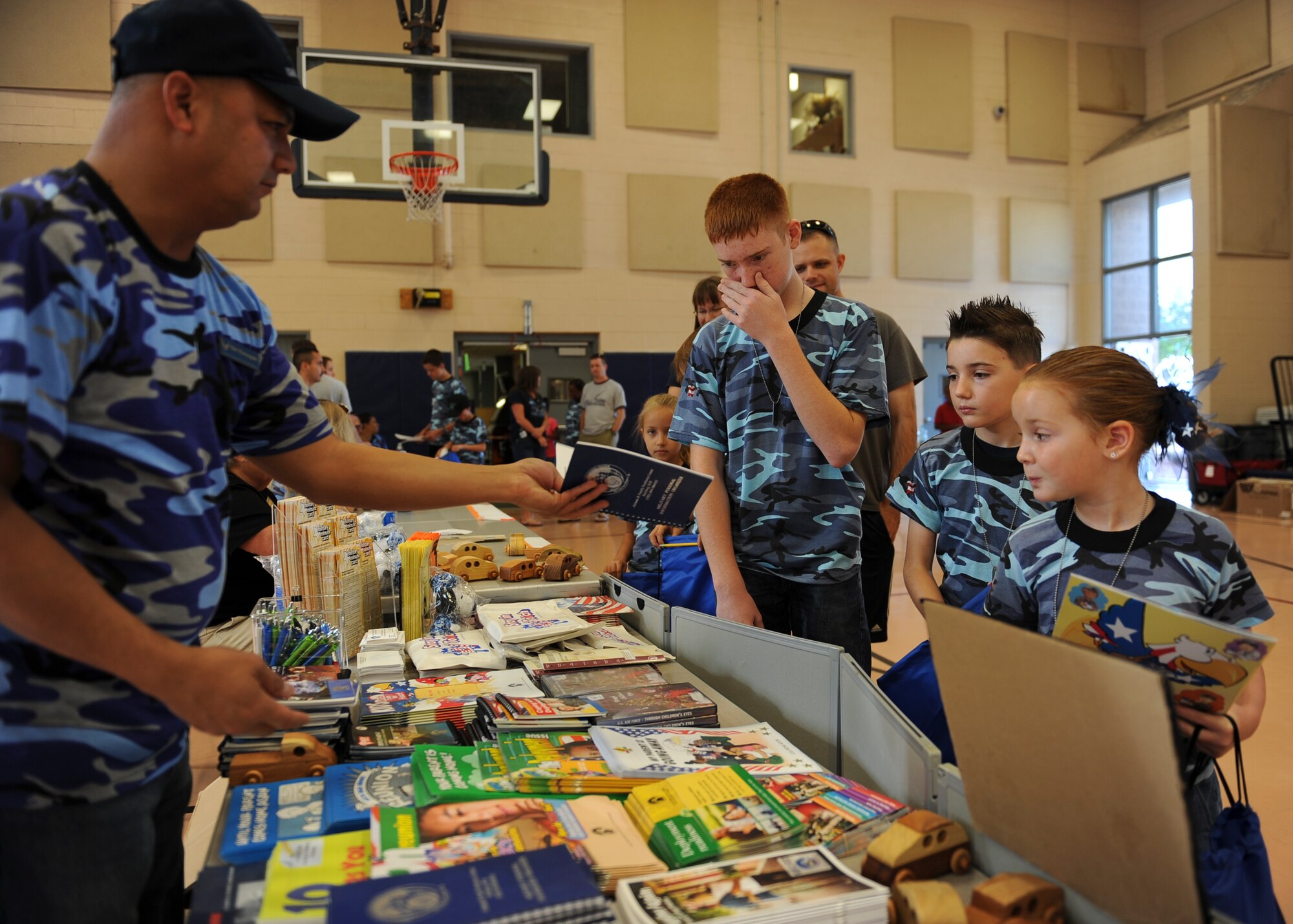 A representative from the Creech Airman and Family Readiness Center hands “deploying” children an informational book as they process through a simulated deployment line during the Nellis and Creech Kids Deployment at Nellis Air Force Base, Nev., Oct. 11, 2014. More than 90 children in four groups were shown gear, vehicles and supplies their parents would use when deployed. (U.S. Air Force photo by Staff Sgt. Victoria Sneed)