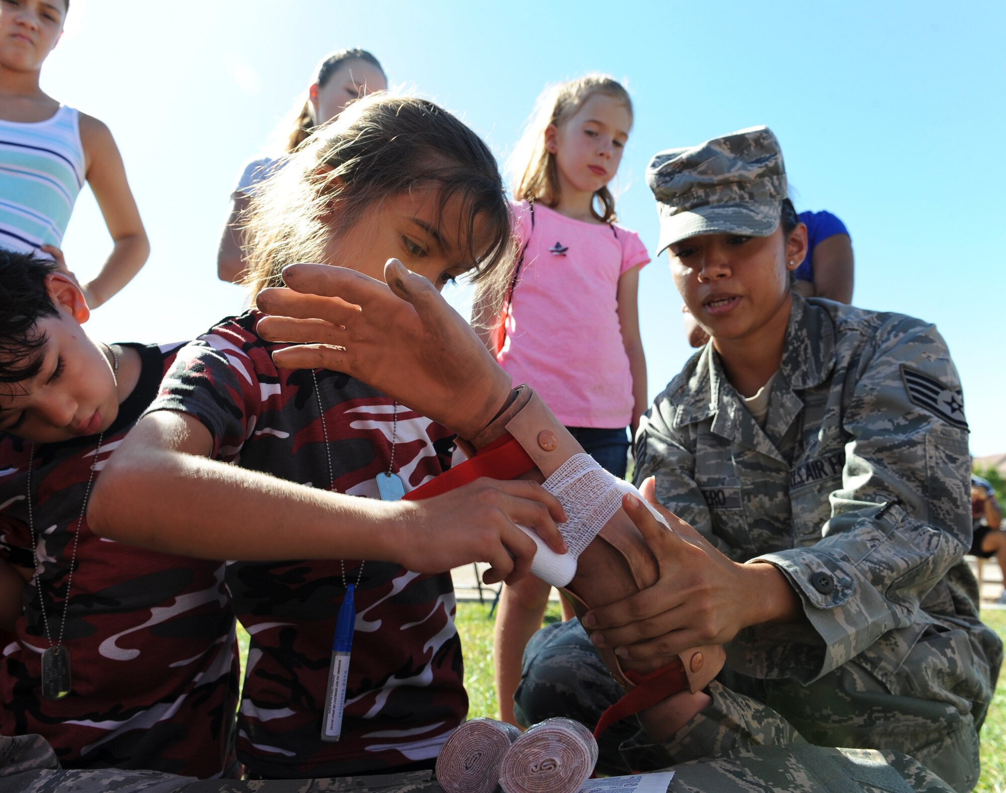 A staff sergeant from the 99th Medical Group shows a child how to bandage an injury on a first-aid dummy during the Nellis and Creech Kids Deployment at Nellis Air Force Base, Nev., Oct. 11, 2014. Children were shown skills, vehicles and gear typically used to give them a better understanding of what their parents go though in preparation for a deployment. (U.S. Air Force photo by Staff Sgt. Victoria Sneed)