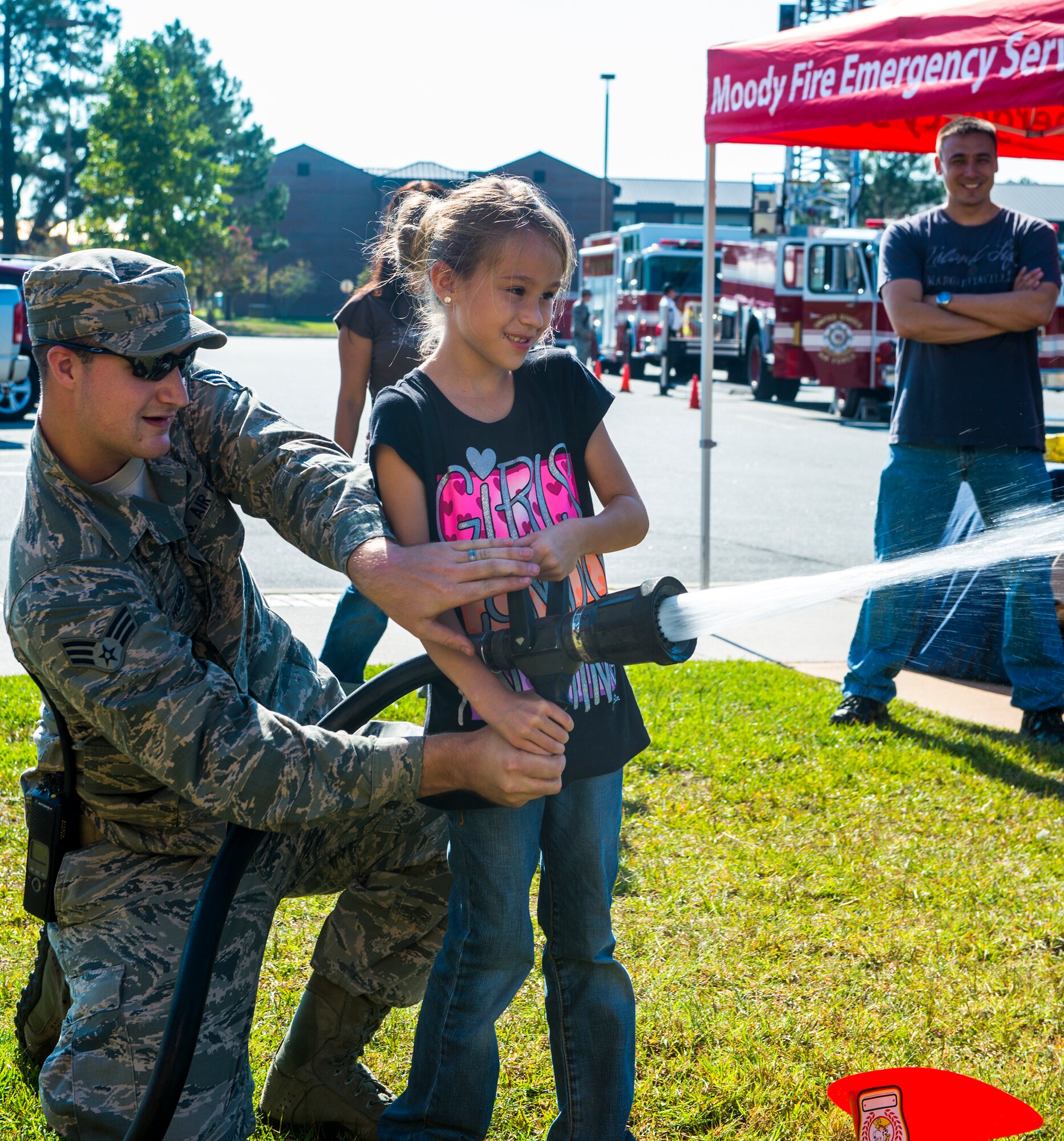 U.S. Air Force Senior Airman Joshua Humes, 23d Civil Engineer Squadron firefighter and Miranda Crane, niece of Senior Master Sgt. Alfred Venditti, 23d Maintenance Group, spray a fire hose during  the Fire Prevention Week Open House Oct. 11, 2014, at Moody Air Force Base, Ga. The theme for this year’s National Fire Prevention Week was “Working Smoke Alarms Save Lives: Test Yours Every Month.” (U.S. Air Force photo by Airman 1st Class Ceaira Tinsley/Released)