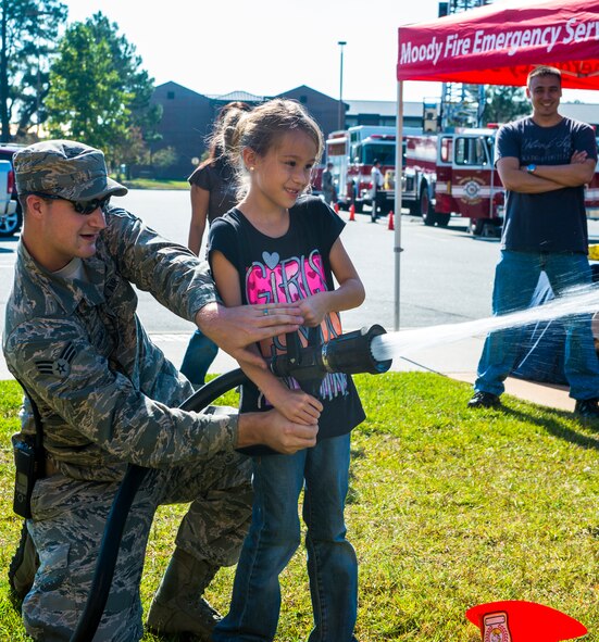 U.S. Air Force Senior Airman Joshua Humes, 23d Civil Engineer Squadron firefighter and Miranda Crane, niece of Senior Master Sgt. Alfred Venditti, 23d Maintenance Group, spray a fire hose during  the Fire Prevention Week Open House Oct. 11, 2014, at Moody Air Force Base, Ga. The theme for this year’s National Fire Prevention Week was “Working Smoke Alarms Save Lives: Test Yours Every Month.” (U.S. Air Force photo by Airman 1st Class Ceaira Tinsley/Released)