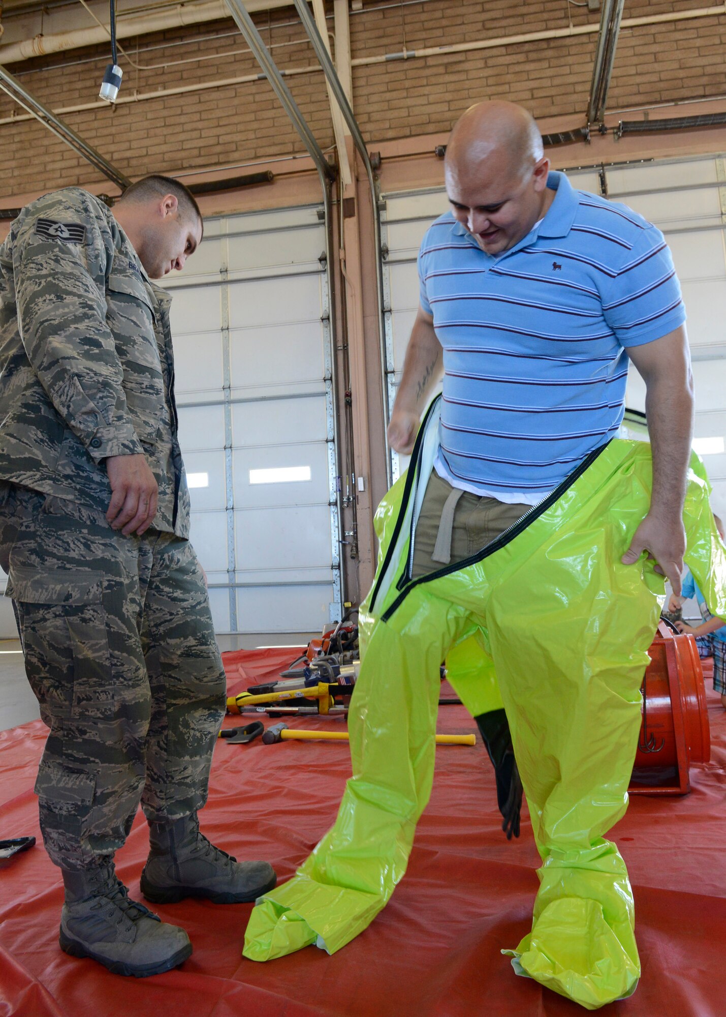 Staff Sgt. Daniel Braitman, 56th CES Fire Services firefighter, shows Alexander Ahlstrom, 308th Aircraft Maintenance Unit crew chief, how to suit-up in a hazard suit Saturday during the 2014 Fire Prevention Week Open House at Luke Air Force Base. October’s fire prevention week reminds people of the dangers and destructive power fire holds when it burns out of control. This year the emphasis was on in-home smoke detectors. (U.S. Air Force photo/Senior Airman Devante Williams)