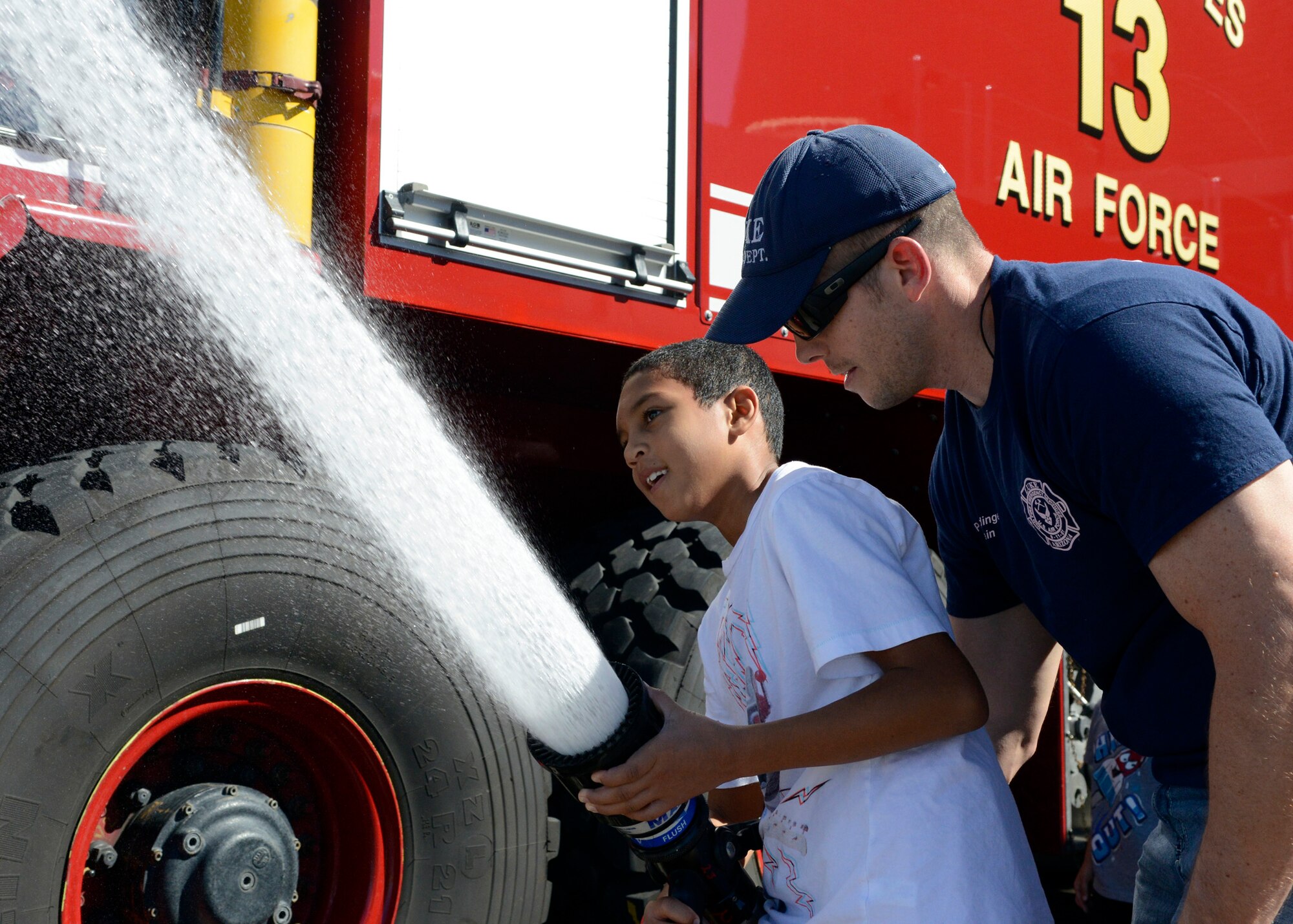 Paul Haidinger, 56th Civil Engineer Squadron Fire Services fire captain, shows Branden Rowe Jr., 10, son of Staff Sgt. Brandon Rowe, 56th Operations Support Squadron aircrew flight equipment NCO in charge, how to control a fire hose Saturday during the 2014 Fire Prevention Week Open House at Luke Air Force Base. Along with the parade, events included demonstrations, fire prevention information, Sparky the Fire Dog and friends. (U.S. Air Force photo/Senior Airman Devante Williams)