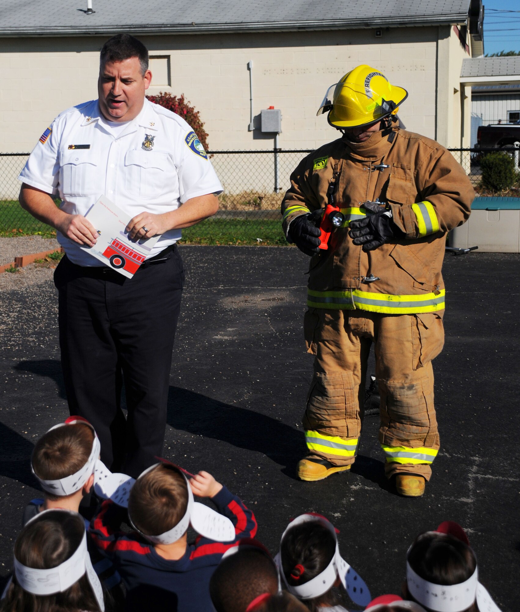 John P. Schultz, Asst. Chief, Fire Prevention,and Jose Vasquez, firefighter, 914th Mission Support Group, show children firefighter equipment at a local school, October 9 2014. Shultz and Vasquez were reminding the children who to look for in an emergency. (U.S. Air Force Photo by Staff Sgt. Matthew Burke)