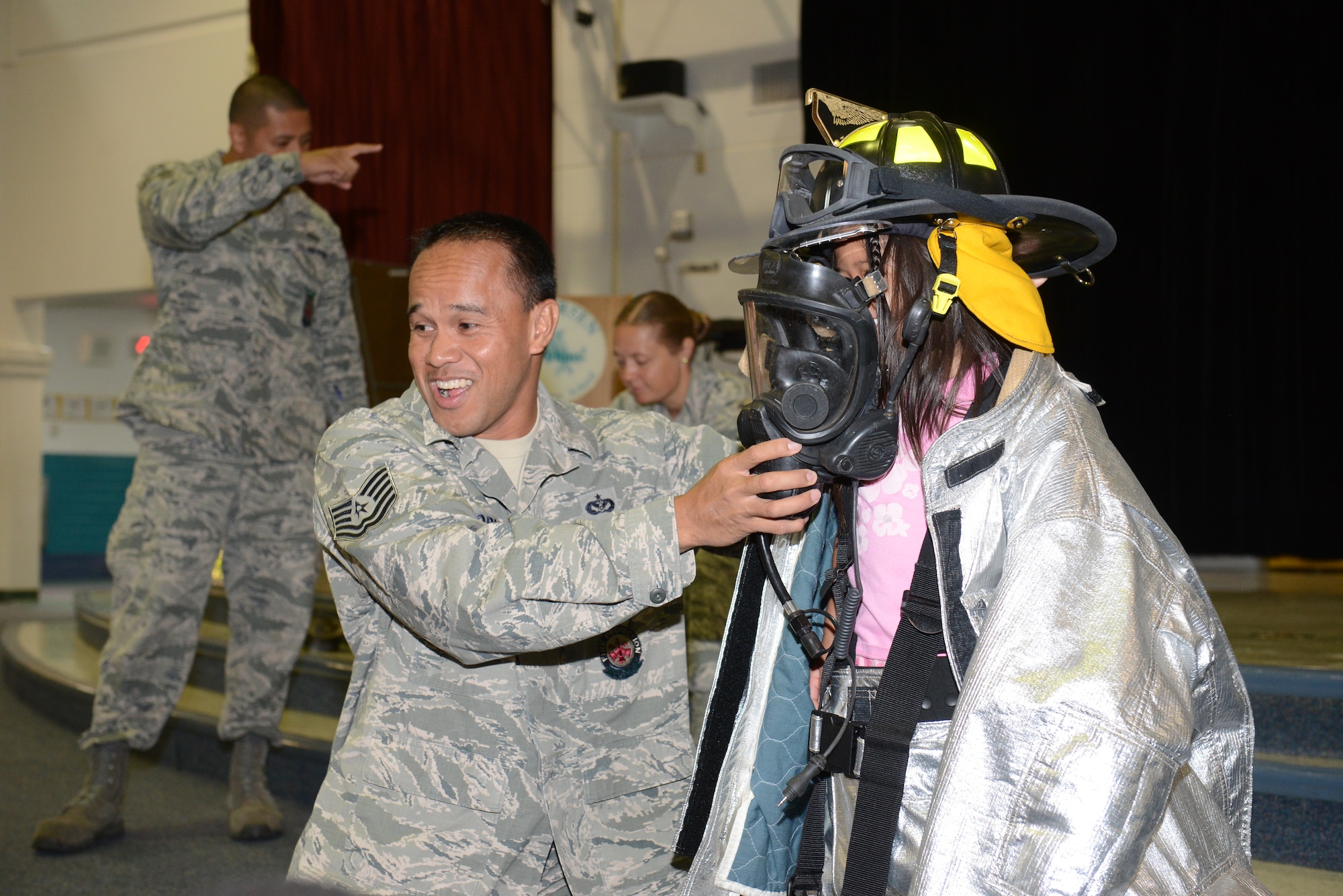 Tech Sgt. Arnel Dorn 36th Civil Engineer Squadron, Firefighter helps a student from Andersen Elementary School put on a gas mask on Andersen Air Force Base, Guam Oct. 8, 2014.The 36th CES visited the elementary school part of Fire Prevention week to raise awareness. (U.S. Air Force photo by Airman 1st Class Adarius Petty/Released)