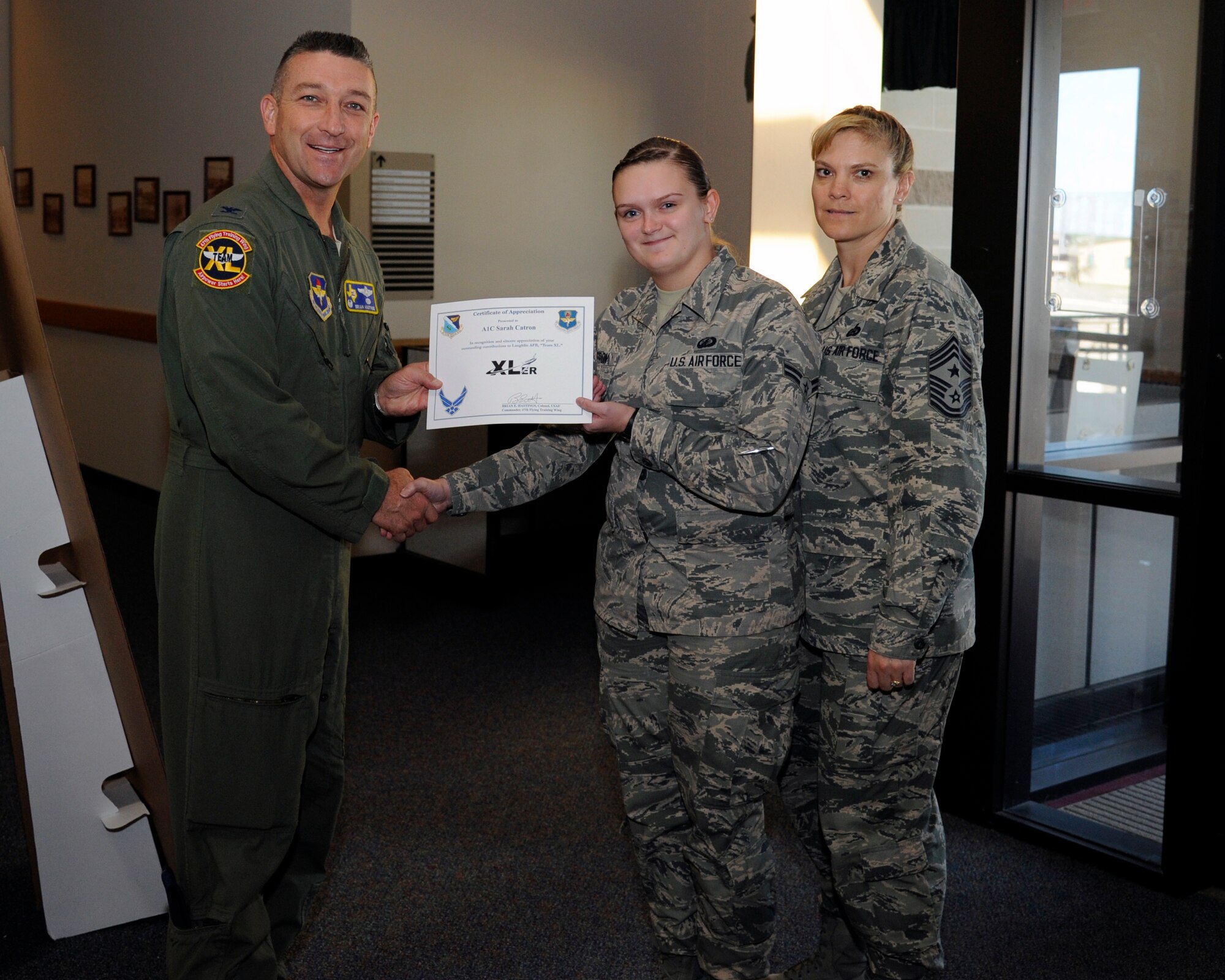 Airman 1st Class Sarah Catron, center, 47th Comptroller Squadron financial services technician, poses with Col. Brian Hastings, left, 47th Flying Training Wing commander, and Chief Master Sgt. Teresa Clapper, right, 47th FTW command chief, after being presented the XLer of the week award here Oct. 15, 2014. The XLer is a weekly award chosen by wing leadership and is presented to those who consistently make outstanding contributions to their unit and Laughlin. (U.S. Air Force photo by Airman 1st Class Jimmie D. Pike)(Released)
