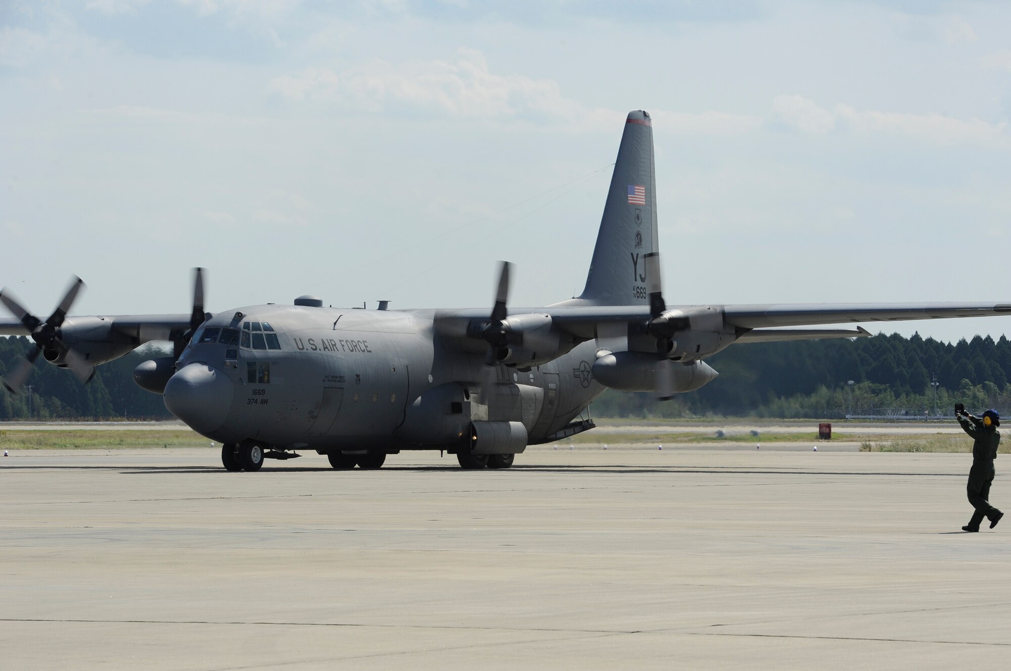 A member of the 5th Air Wing Japan Air Self-Defense Force guides a C-130 Hercules after it landed on Nyutabaru Air Base, Japan, Oct. 16, 2014. The C-130 is from the 374th Airlift Wing at Yokota Air Base, Japan, and dropped off supplies in preparation for the start of the Aviation Training Relocation Program between U.S. and Japanese forces. (U.S. Air Force photo by Senior Airman Marcus Morris/Released)