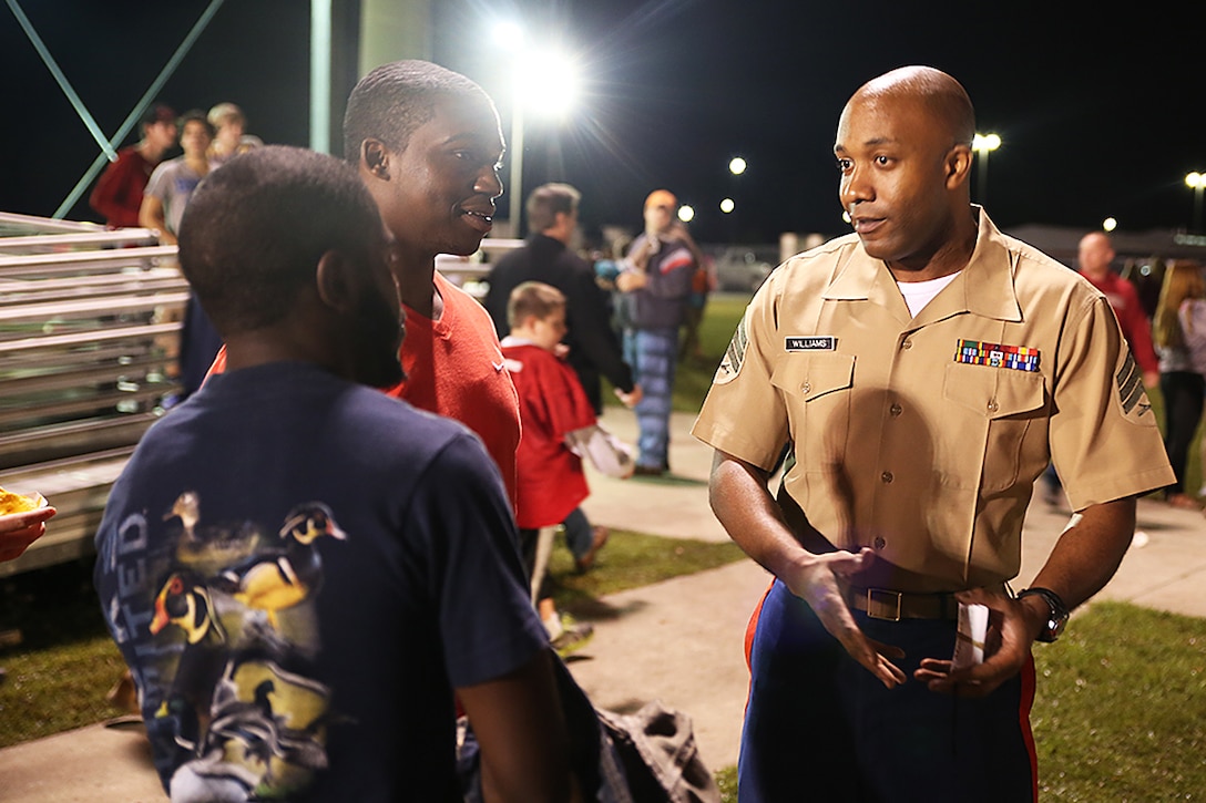 Sgt. Jerry N. Williams, non-commissioned officer in charge from Recruiting Substation Myrtle Beach, Recruiting Station Columbia, communicates with a couple of high school students during the football game between South Florence High School and Carolina Forest High School Oct. 17, 2014, in Myrtle Beach, S.C. (Official Marine Corps photo by Cpl. John-Paul Imbody)