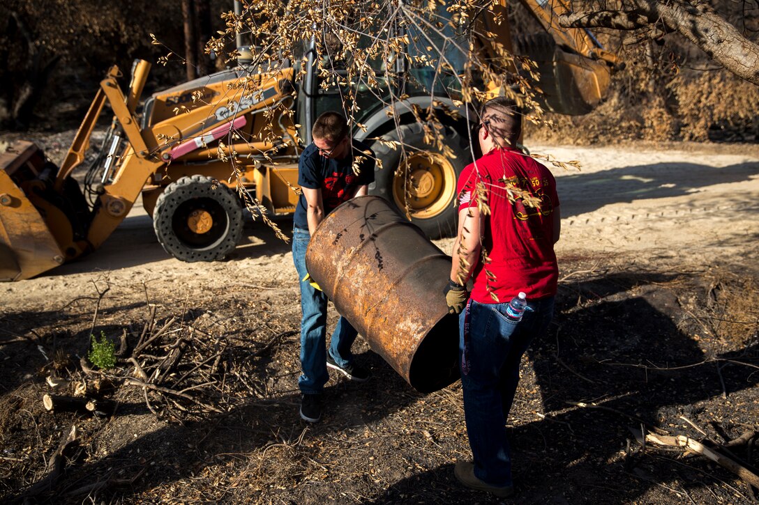 Lance Cpl. Jarrett Scoggins, left, and Lance Cpl. Tyler Eddy, both airframe mechanics with Marine Light Attack Helicopter Squadron (HMLA) 169, carry a metal barrel out of a fire-damaged area during a cleanup in Carlsbad, Oct. 18. Local volunteers and Marines assisted in cleaning the area to help in bringing its ecosystem back to normal. 