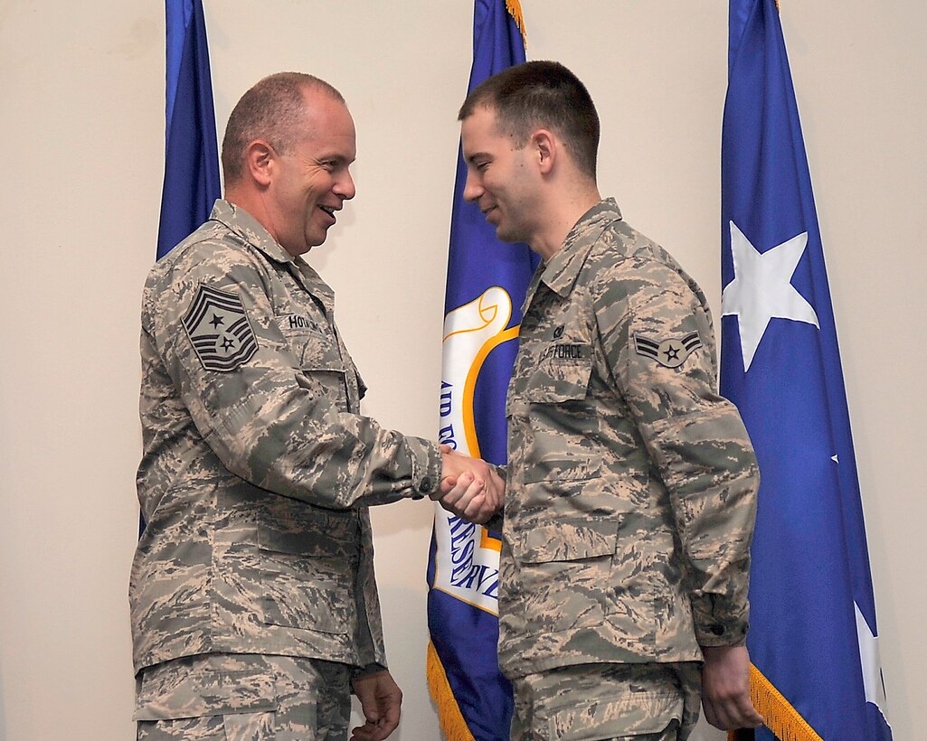 During an “All Call” he hosted, Air National Guard Command Chief Master Sgt. James Hotaling gives his coin to Airman 1st Class Tyler Turnmire, an air tasking order technician from the 601st Air and Space Operations Center. The Chief brought Turnmire, who graduated basic training in May, up to the stage to remind audience members the pride and commitment to the profession of arms present during basic training should remain throughout a person’s military career. (Photo by Airman 1st Class Ty Rico Lea)