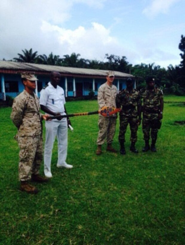 Members of Security Cooperation Team 5B, Special Purpose Marine Air Ground Task Force-Crisis Response-Africa present an oar to Captain Stephane Bullet, the company commander and senior ranking officer for the Cameroonian Naval Commando Company (COPALCO) in Cameroon, Sept. 28, 2014. The team created the oar in Cameroon and wrapped the handles in parachute cord. In the center of the paddle are the ranks of the SCT-5B team members, with the paddle portion holding patches from the Coast Guard, Navy and Marine Corps. SCT-5B worked with the COPALCO on marksmanship, boat operations, and patrolling. (Courtesy Photo)