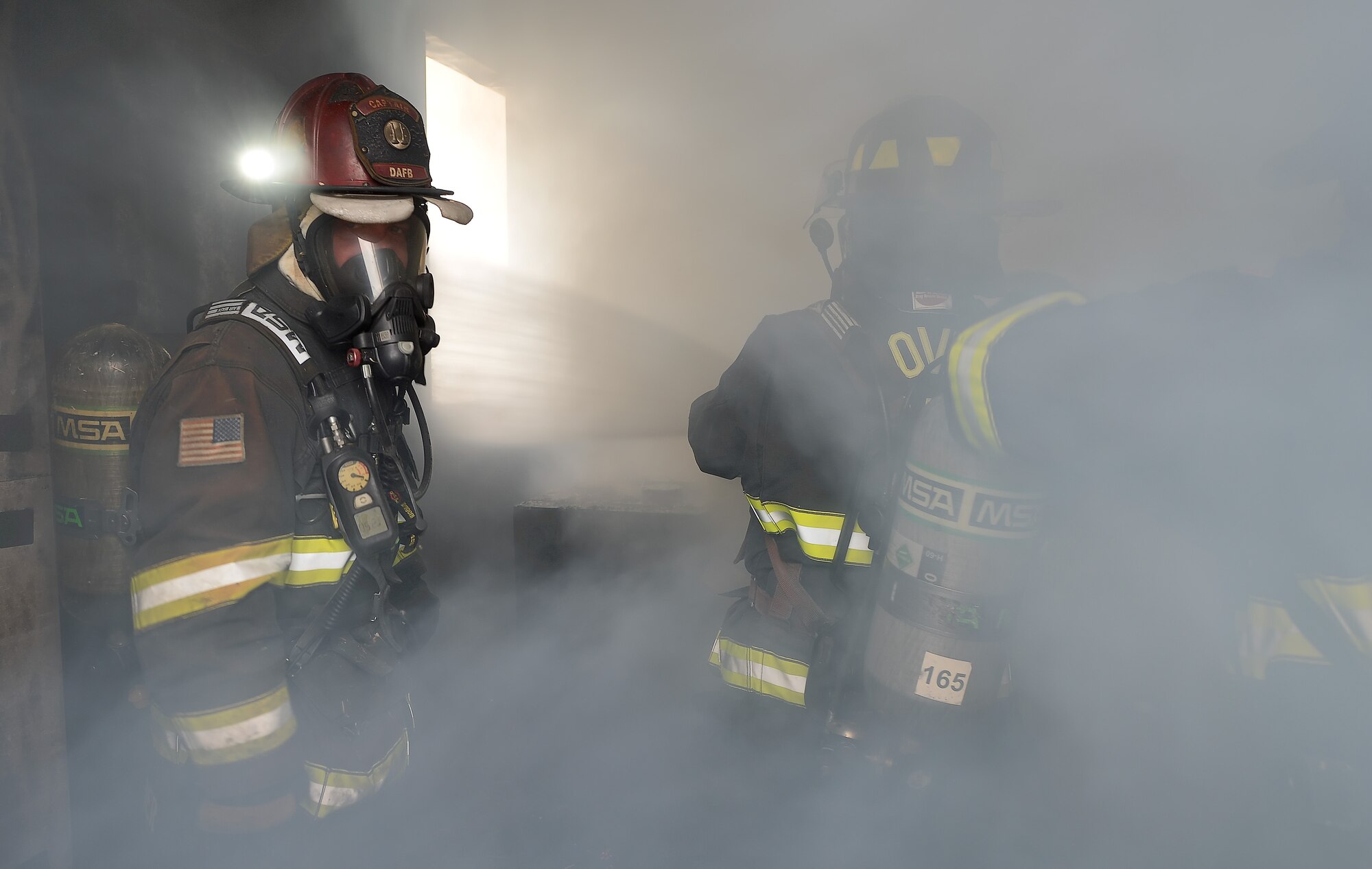 Aaron Weisenberger, 436th Civil Engineer Squadron firefighter, left, monitors the actions of a pair of firefighters as they participate in structural fire training Oct. 20, 2014, at Dover Air Force Base, Del. Smoke can be seen moving toward the window opening through which water is sprayed while the firefighters use hydraulic ventilation to quickly clear the room of smoke. (U.S. Air Force photo/Greg L. Davis)