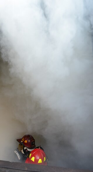 Two firefighter's helmets from the 436th Civil Engineer Squadron Fire Department, are visible surrounded by smoke as they crouch near the floor while positioning themselves to fight a simulated kitchen fire during structural fire training Oct. 20, 2014, at Dover Air Force Base, Del. Getting close to the floor better allows the firefighters to see potential survivors and determine the source of the fire. (U.S. Air Force photo/Greg L. Davis)