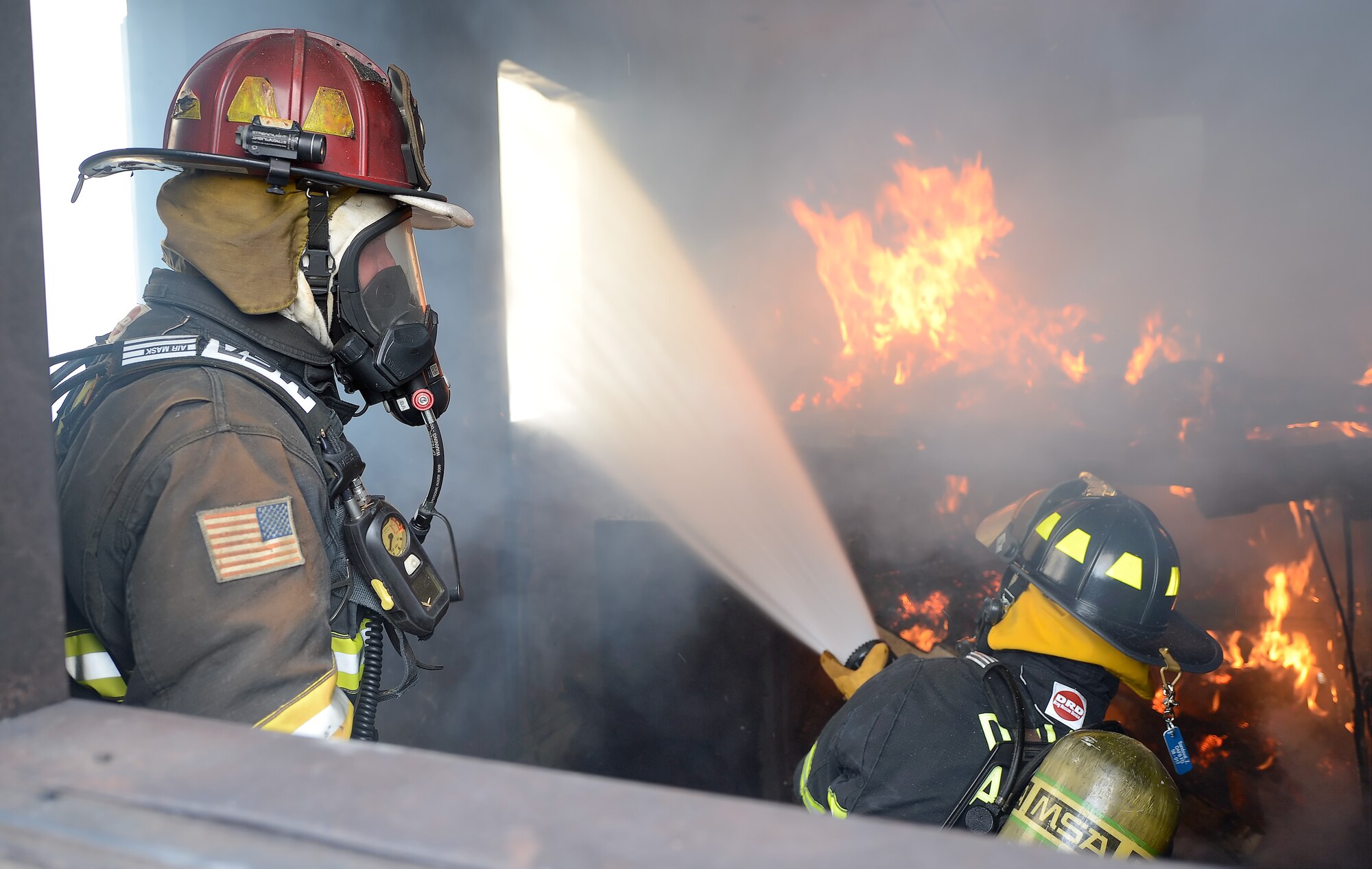 Water is sprayed through a structure window to help remove smoke from a room consumed by fire and smoke so personnel from the 436th Civil Engineer Squadron Fire Department can determine if there is anyone inside during structural fire training Oct. 20, 2014, at Dover Air Force Base, Del. A safety monitor stands by to observe and instruct, as necessary inside the multi-story, specially-built fire training structure. (U.S. Air Force photo/Greg L. Davis) 